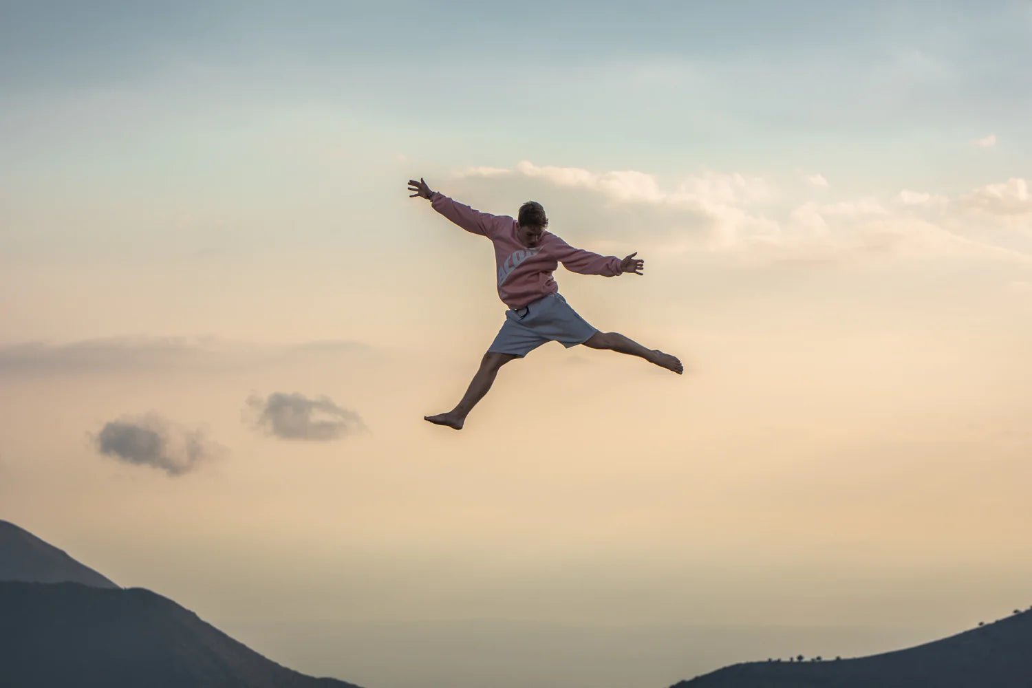 Eine Person, die in die Luft springt und ein rosafarbenes Acon-Sweatshirt in einer griechischen Landschaft trägt
