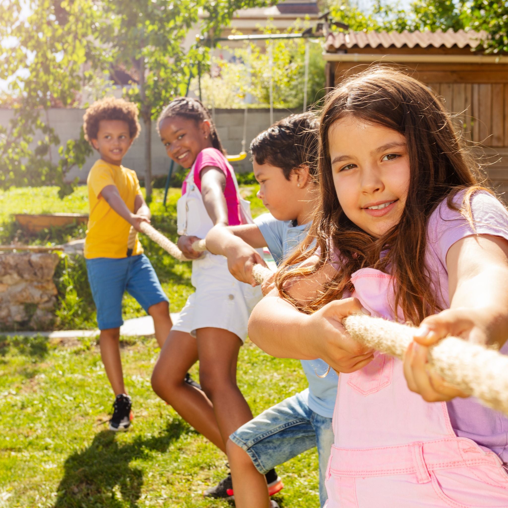 Kinder spielen im Garten Tauziehen, umgeben von fröhlicher Atmosphäre und Spielgeräten. Trampolin Spiele und Ideen.