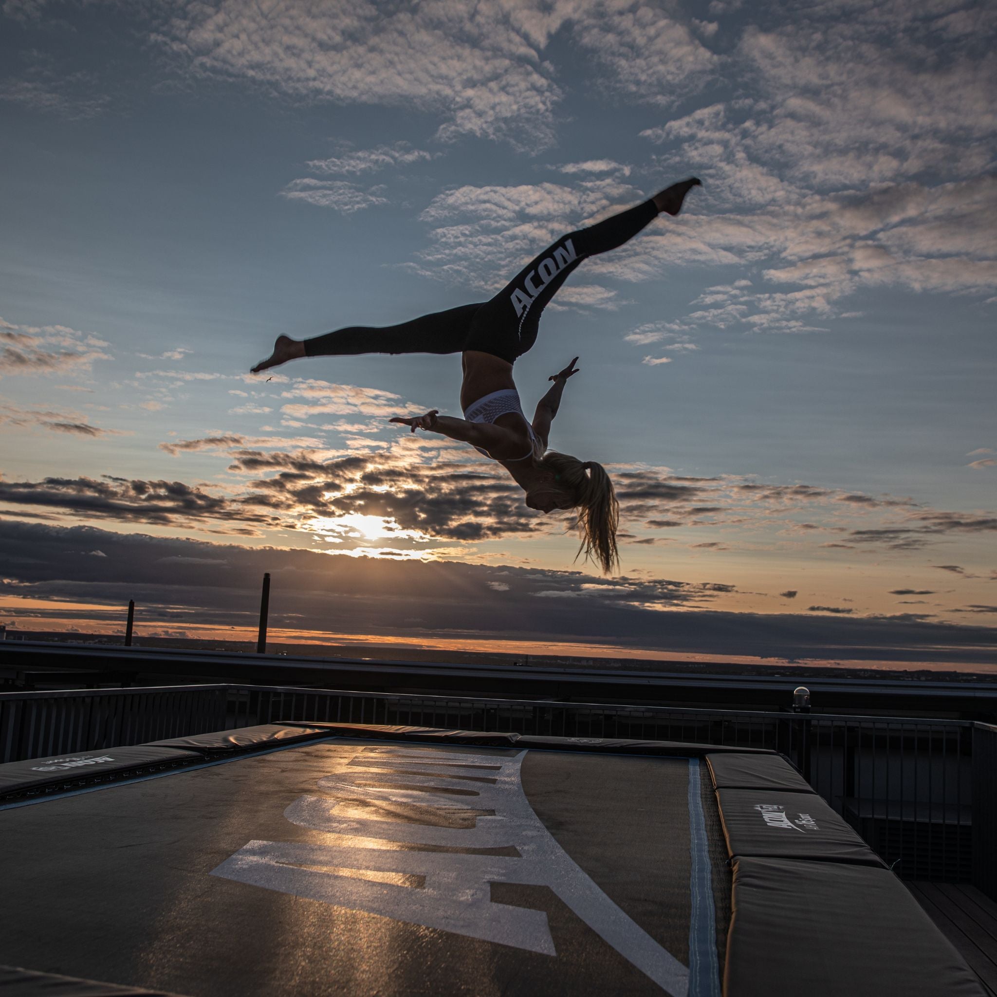 Eine Frau macht einen Flip auf einem Trampolin bei Sonnenuntergang.