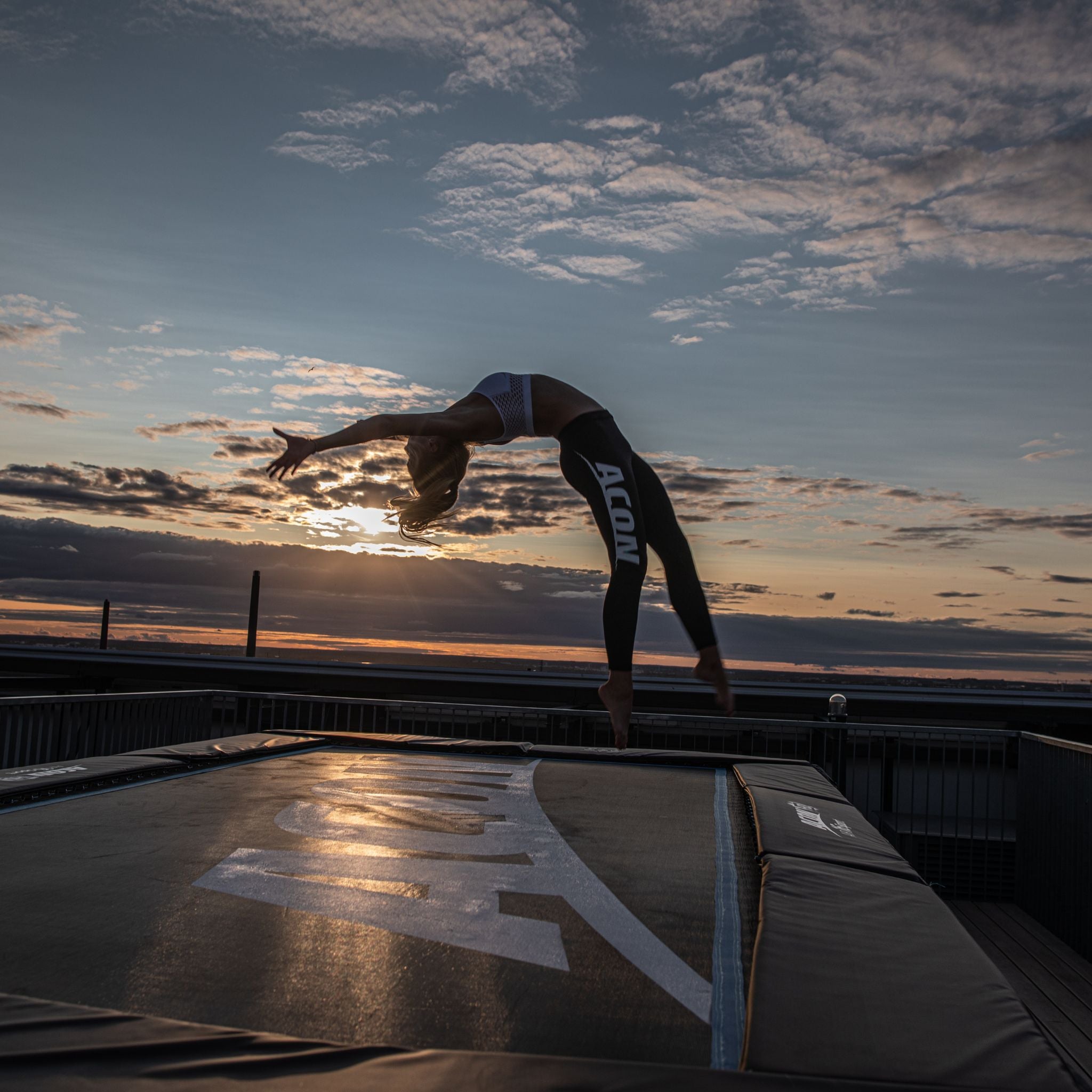 Eine Frau springt auf einem Trampolin und führt einen Flip bei Sonnenuntergang aus.