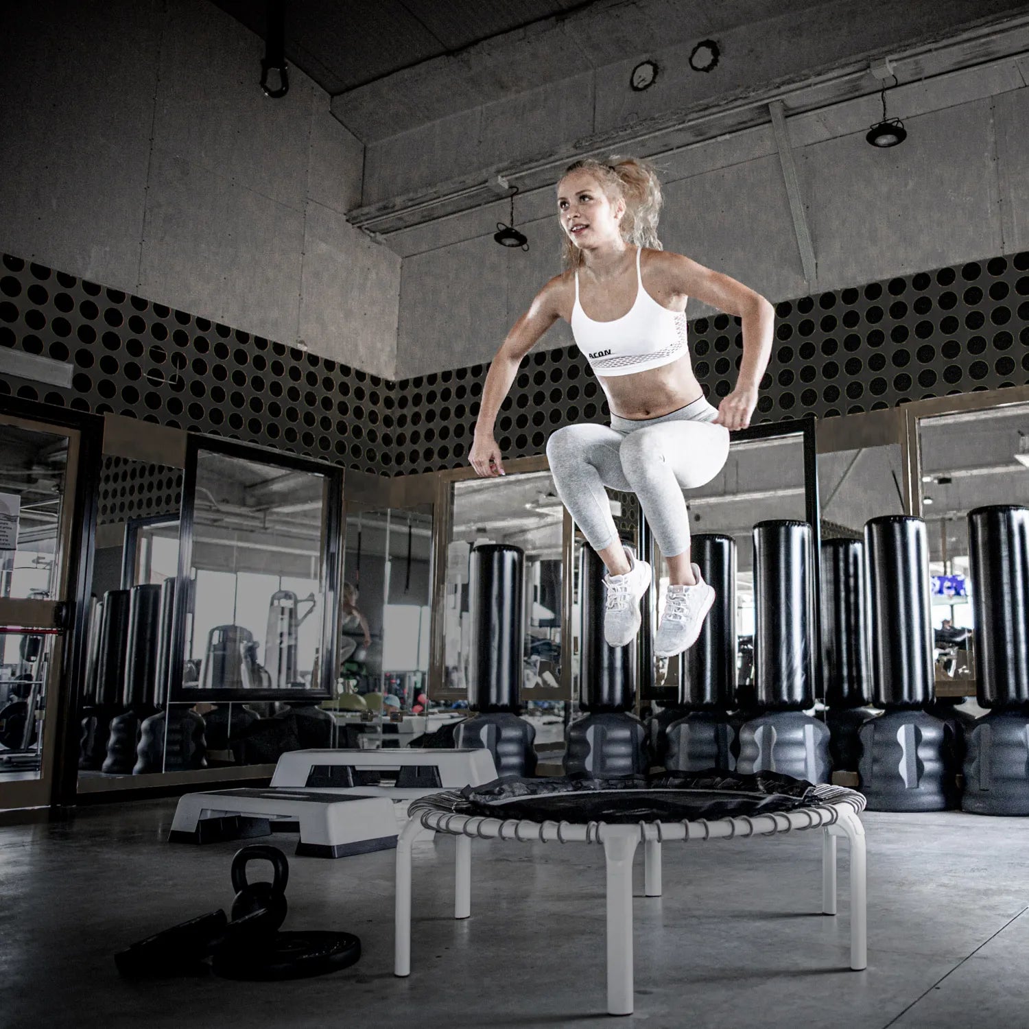 Athlet springt auf dem ACON Fit 1,12 m Runden Rebounder mit Aktiv-Haltestange im Fitnessstudio.