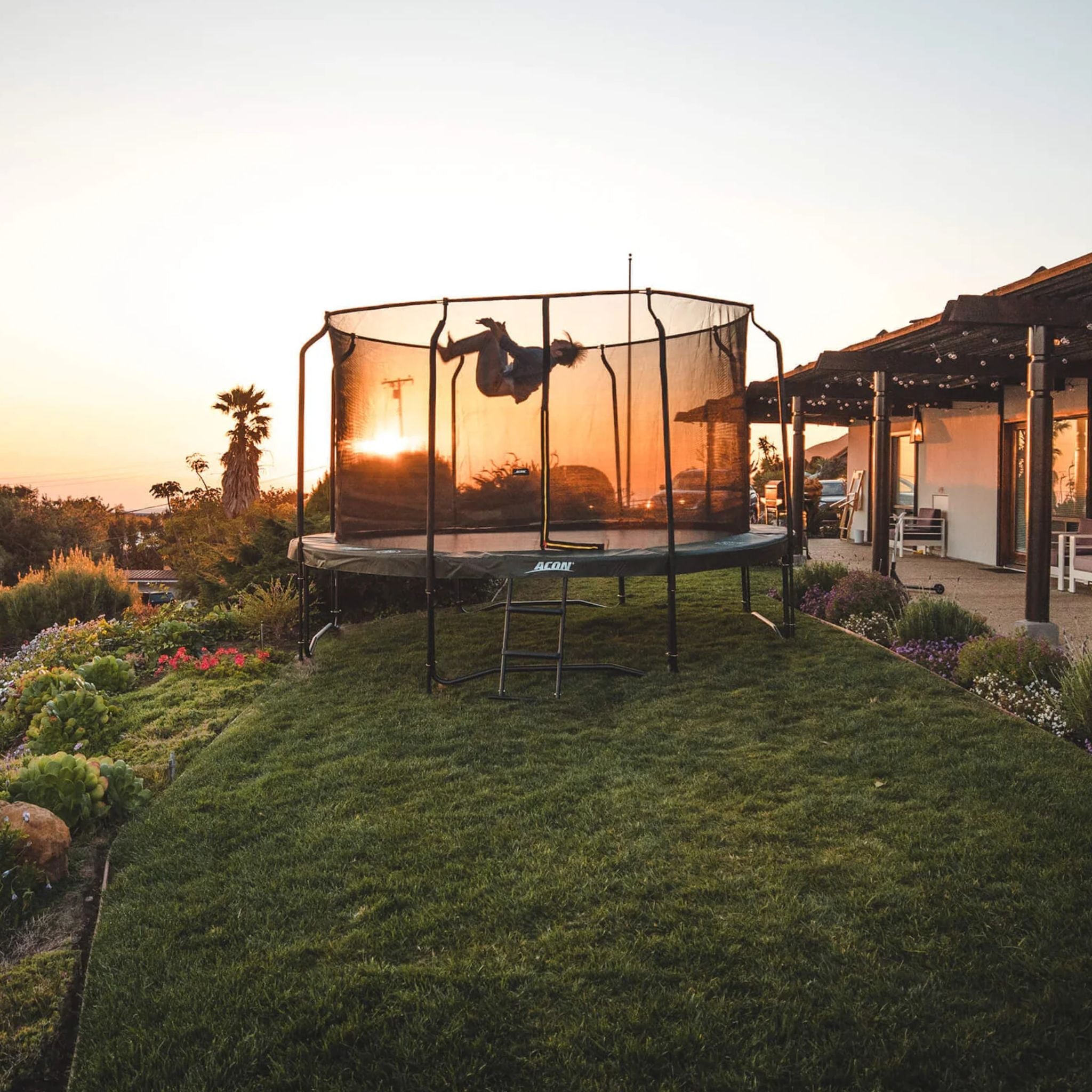 Person springt auf einem Trampolin im Garten. Unter dem Trampolin ist Rasen.