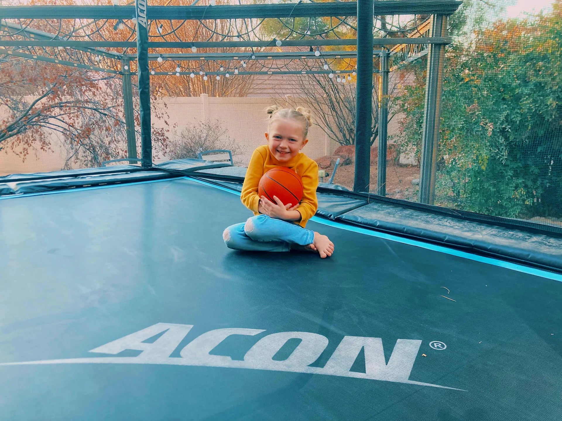 Kind sitzt auf rechteckigem Trampolin mit Basketball