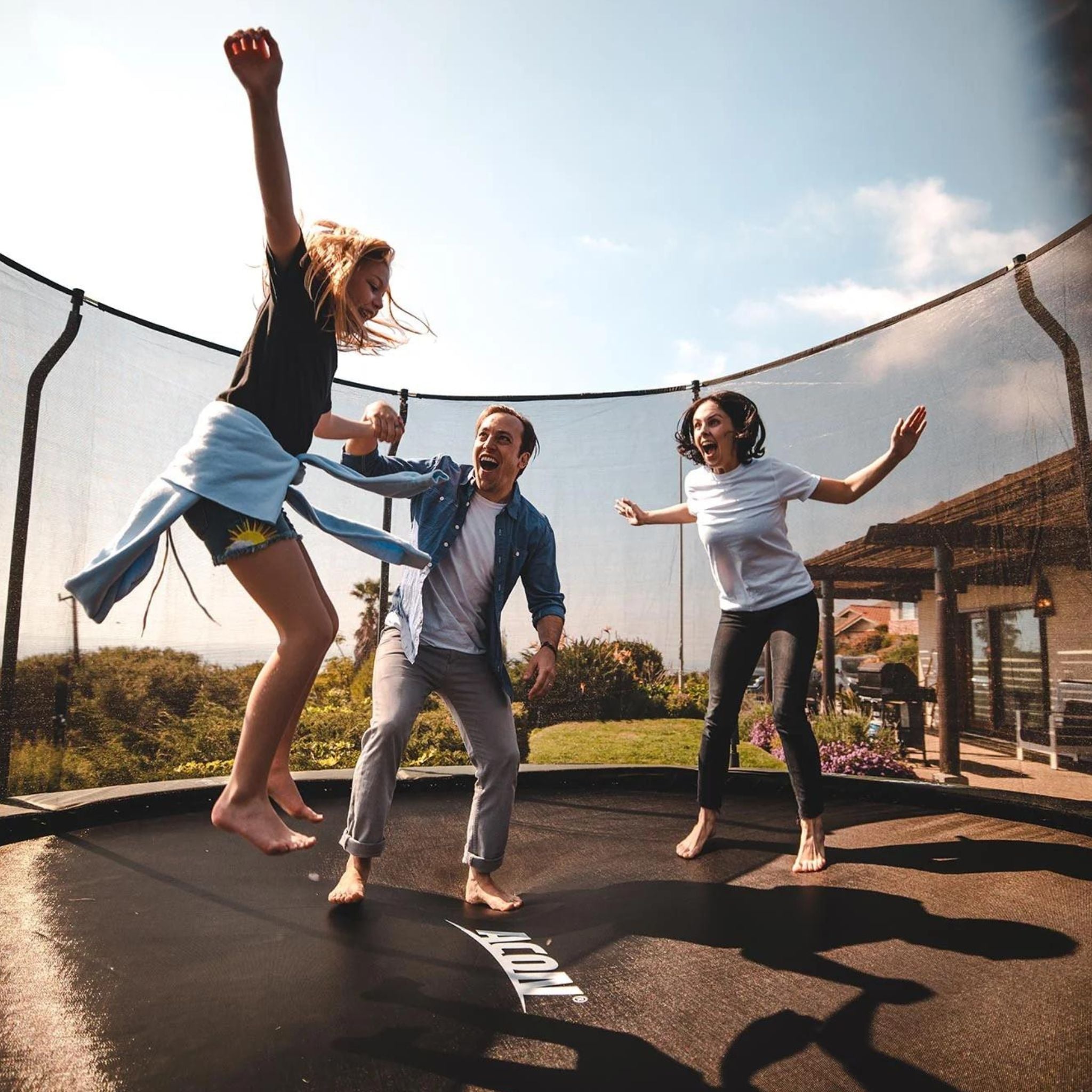 Familie hüpft im Trampolin vor einem Haus. Trampolin Regeln.