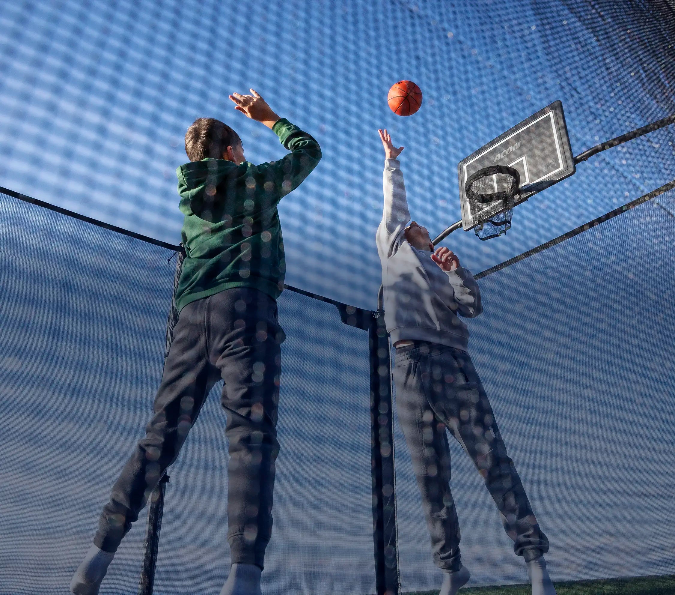Zwei Jungen spielen Basketball auf einem Acon X Trampolin.
