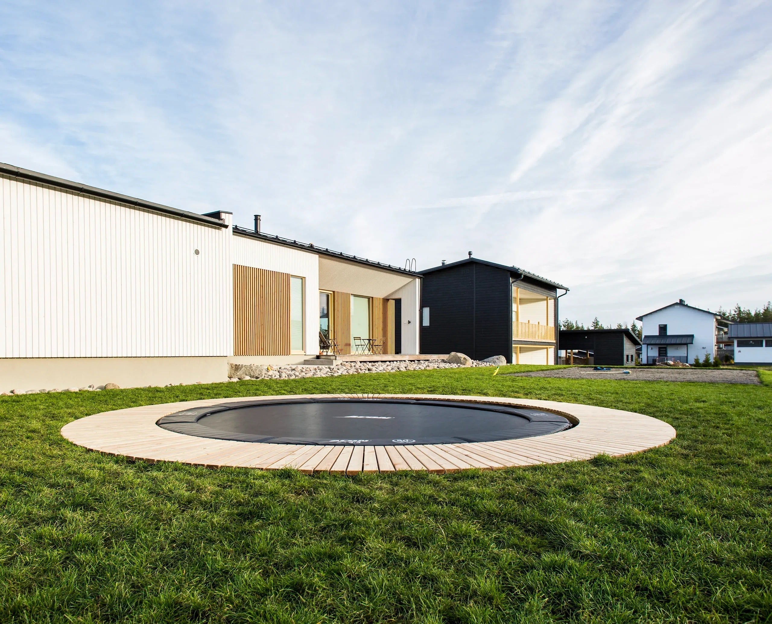 Bodentrampolin bündig im Rasen eines modernen Hauses – Inground Trampolin vs Standtrampolin im Garten