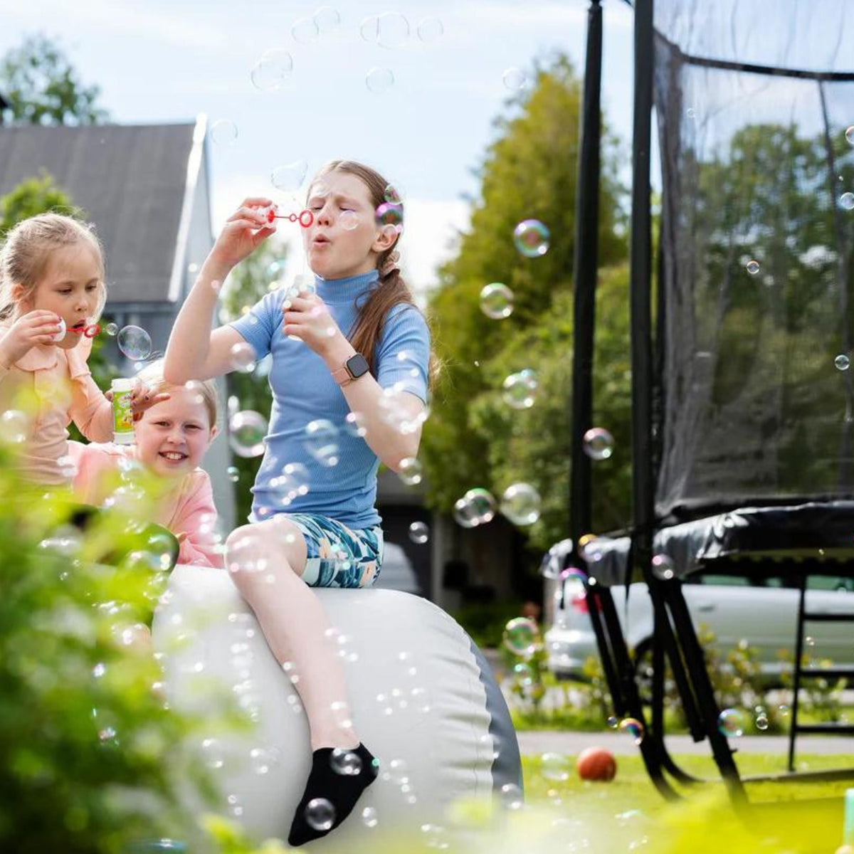 Kinder spielen draussen neben Trampolin. Ab welchem Alter ist Trampolinspringen sicher.