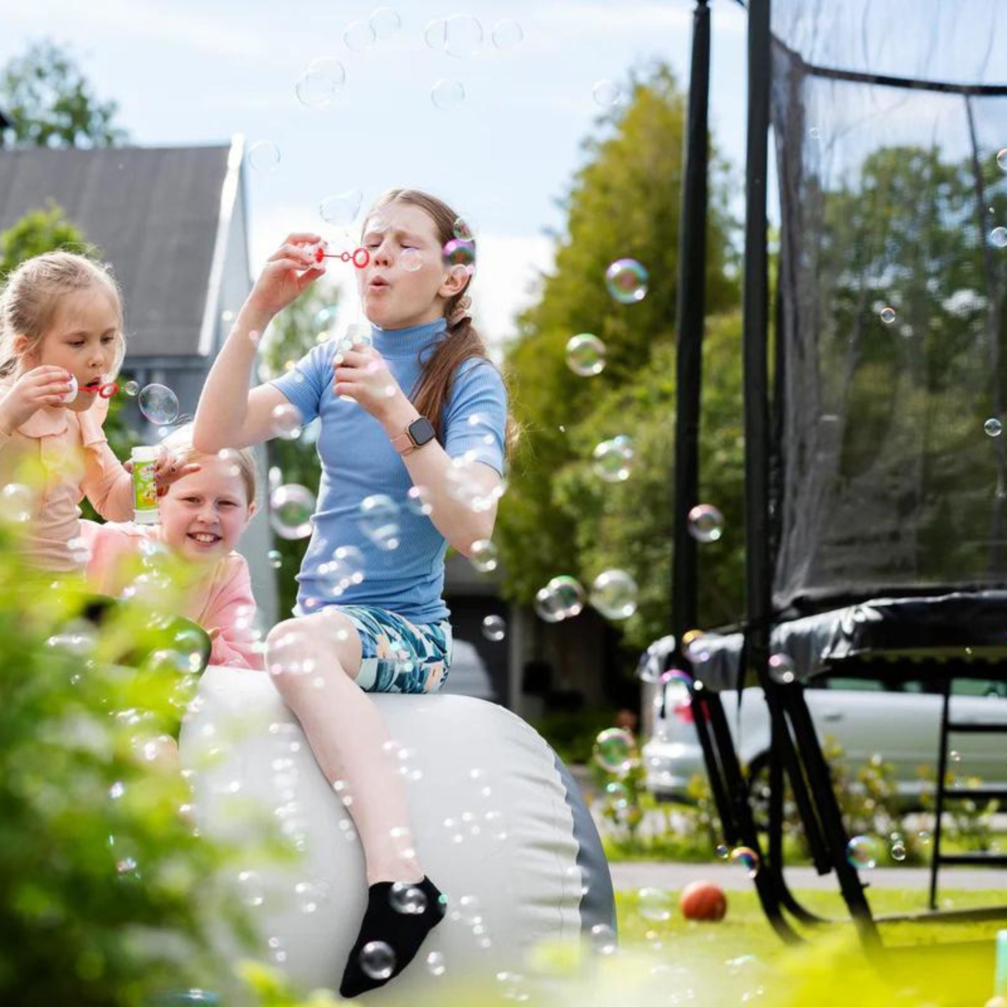 Kinder spielen draussen neben Trampolin. Ab welchem Alter ist Trampolinspringen sicher.