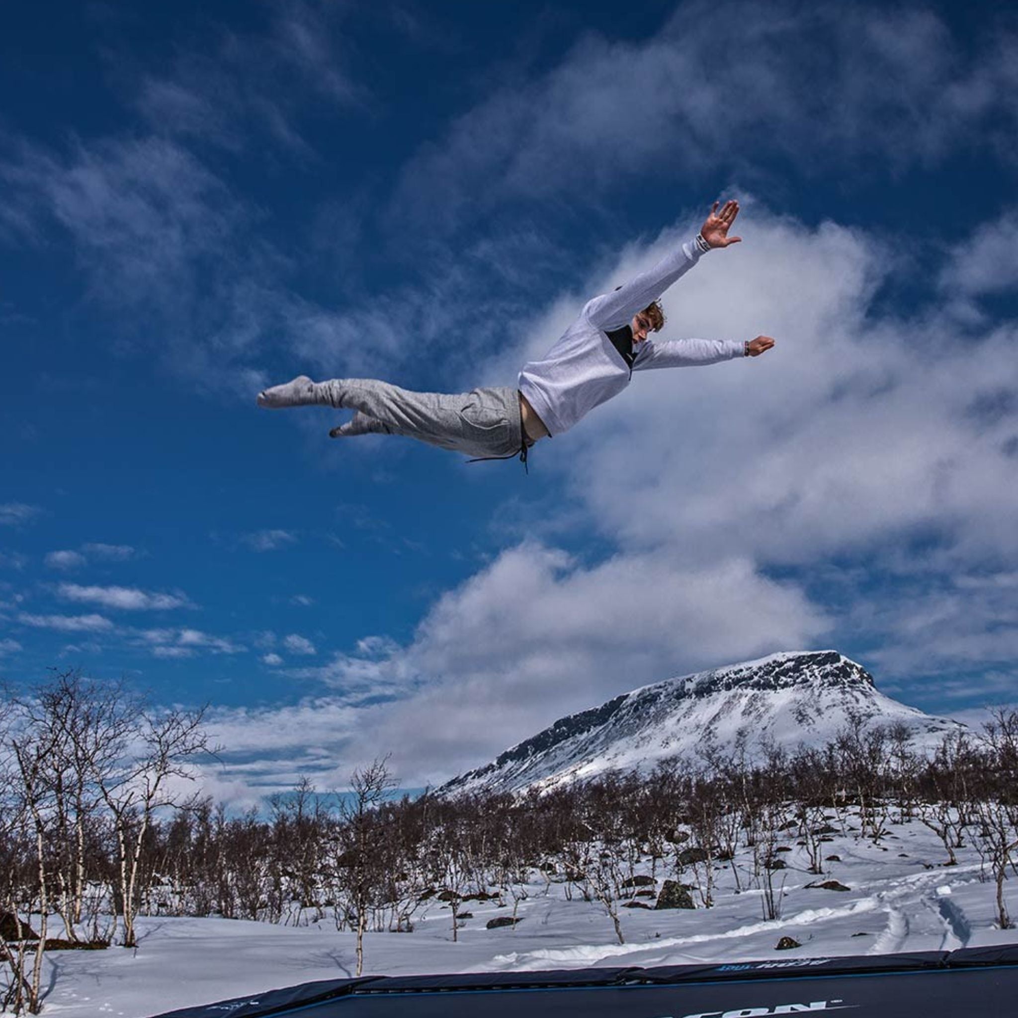 Mann in grauem Jogginganzug springt auf einem Trampolin im Schnee