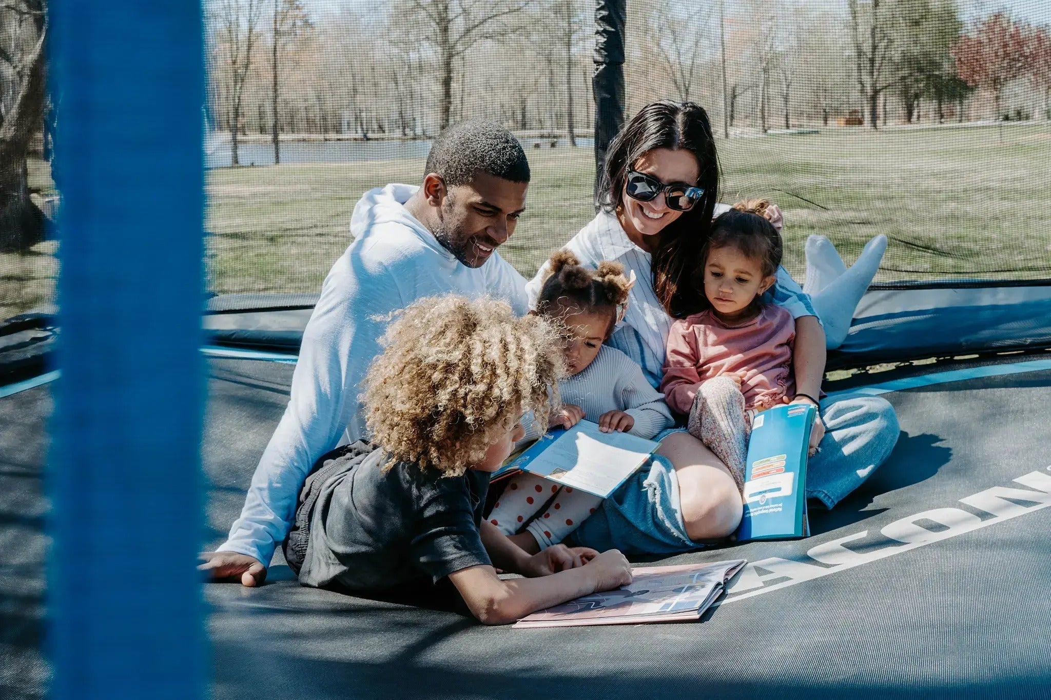 Familie sitzt auf einem Acon-Trampolin und liest gemeinsam im Freien.