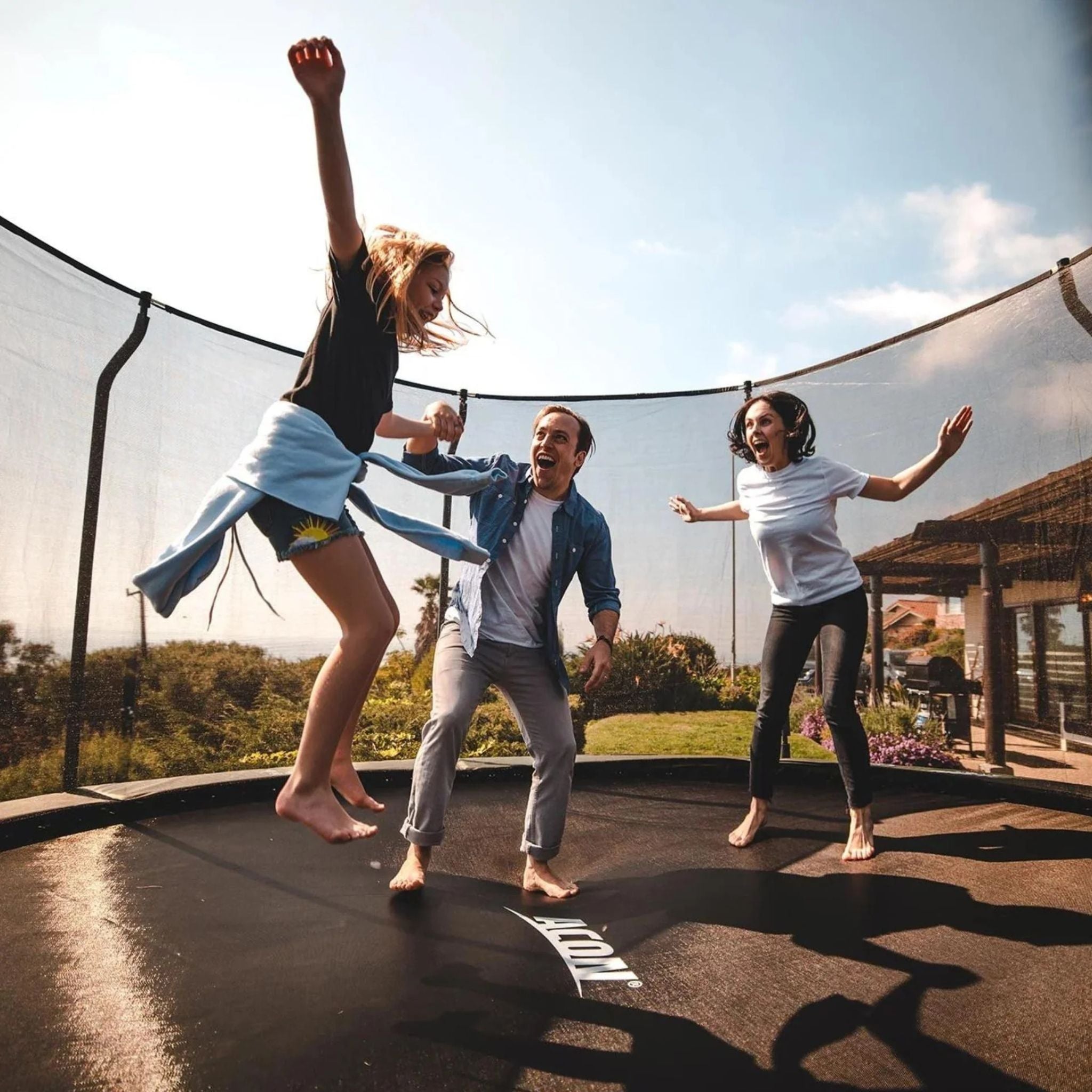 Drei Personen springen fröhlich auf einem Trampolin im Freien.