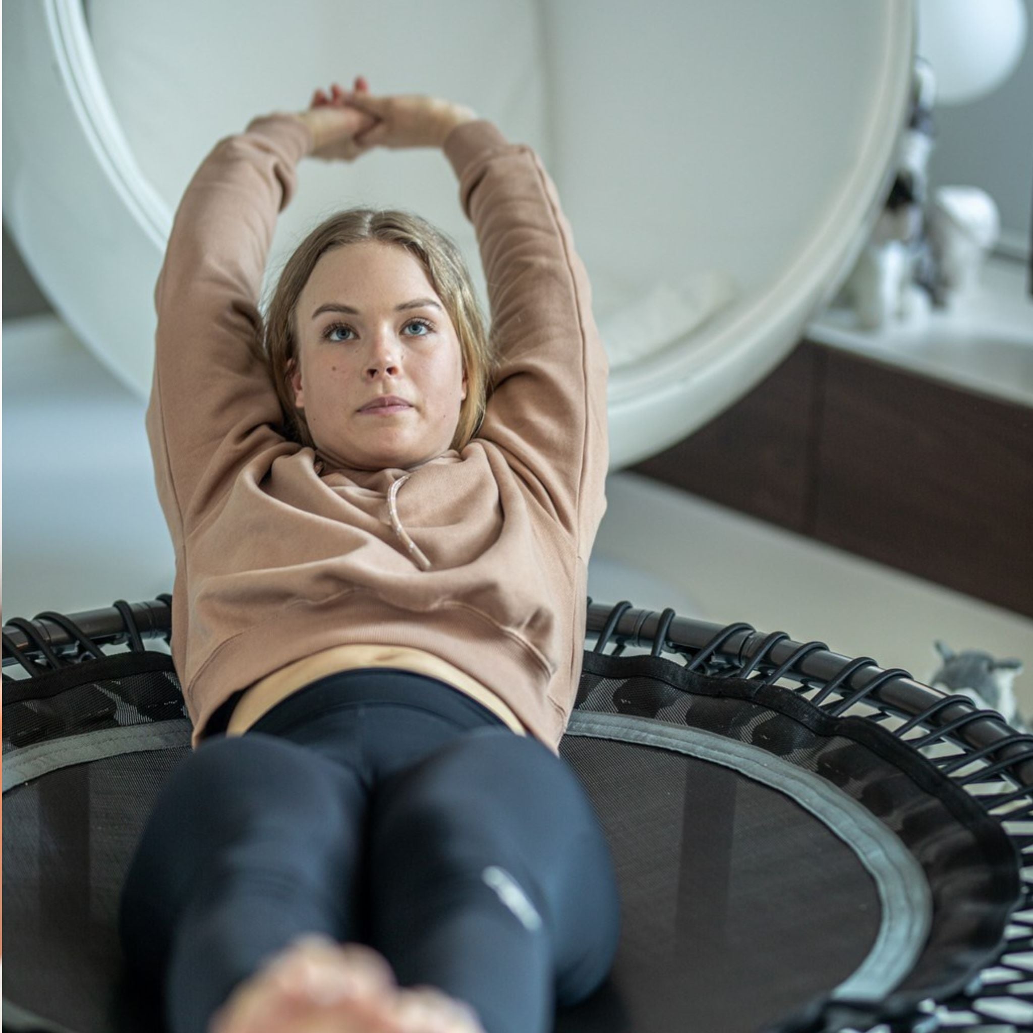 Frau mit beigem Pullover trainiert auf Mini-Trampolin