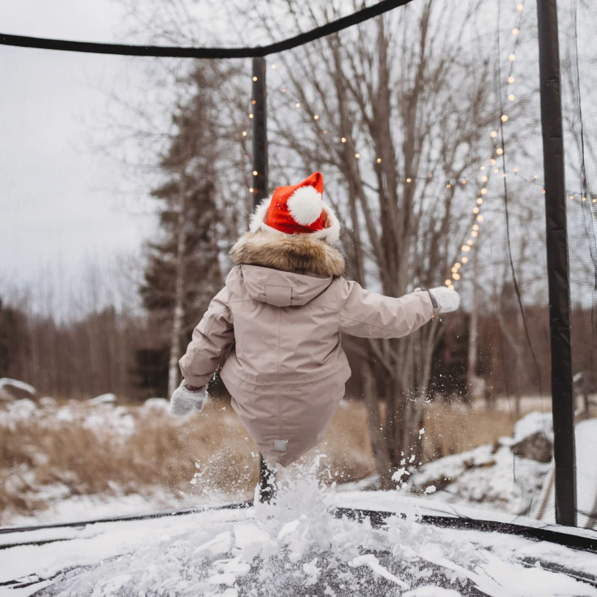 Kind mit Nikolausmütze hüpft auf einem ACON Trampolin im Schnee
