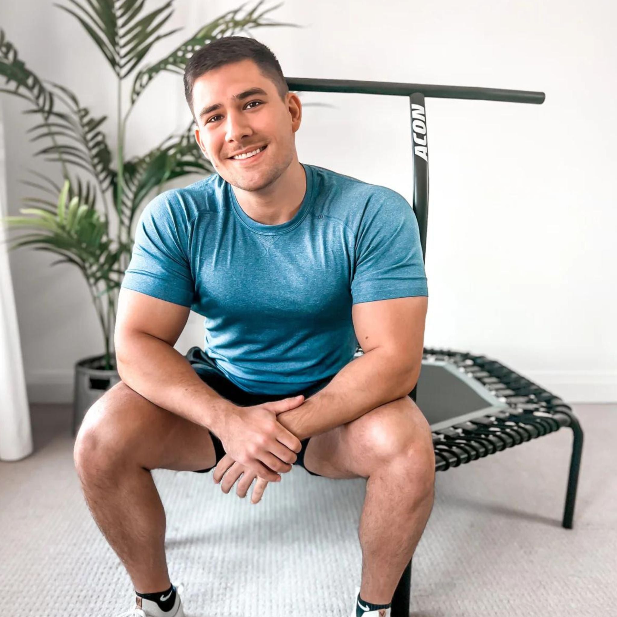 Mann mit blauem T-Shirt sitzt auf einem indoor Trampolin