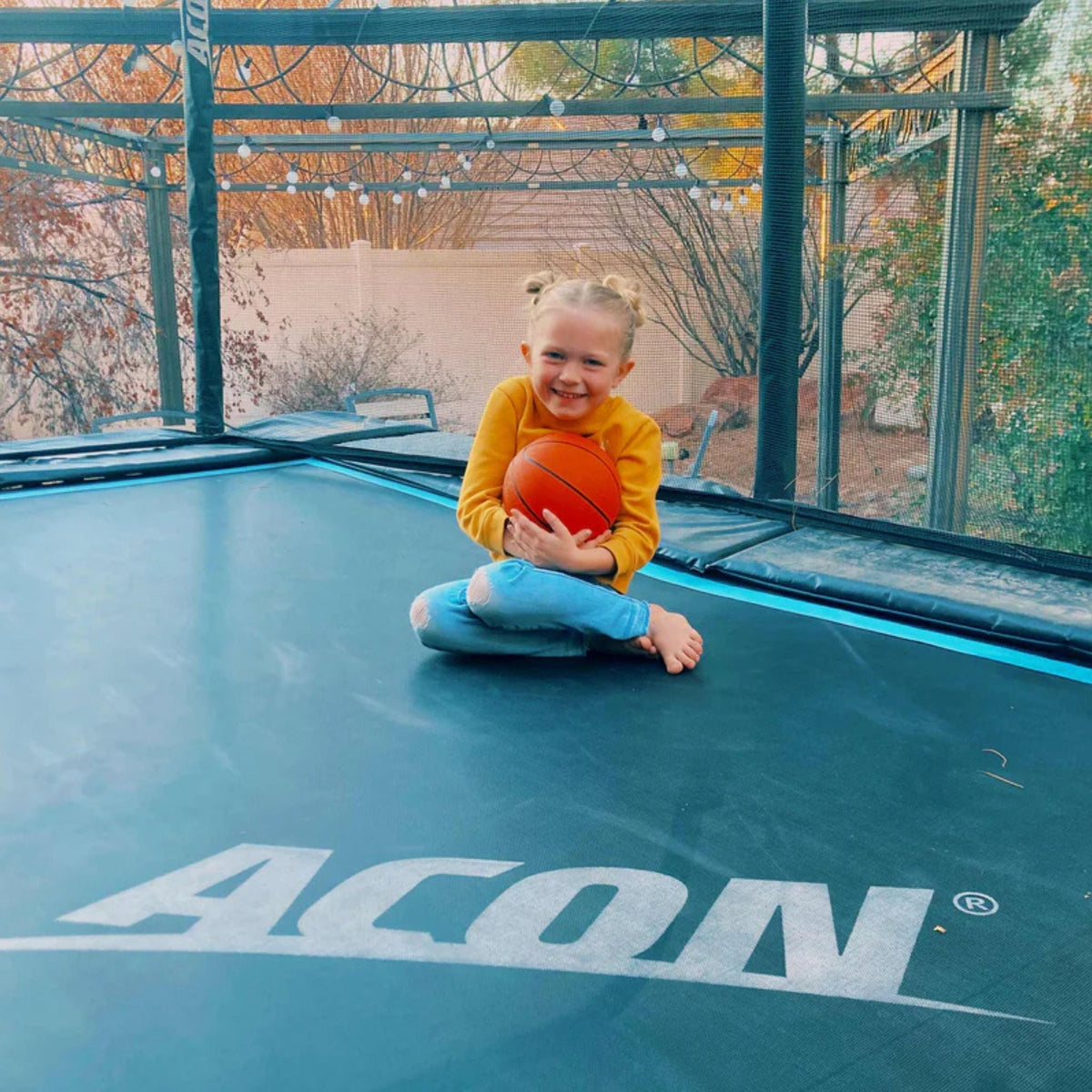 Kind sitzt mit Basketball einem Trampolin mit Lichtern