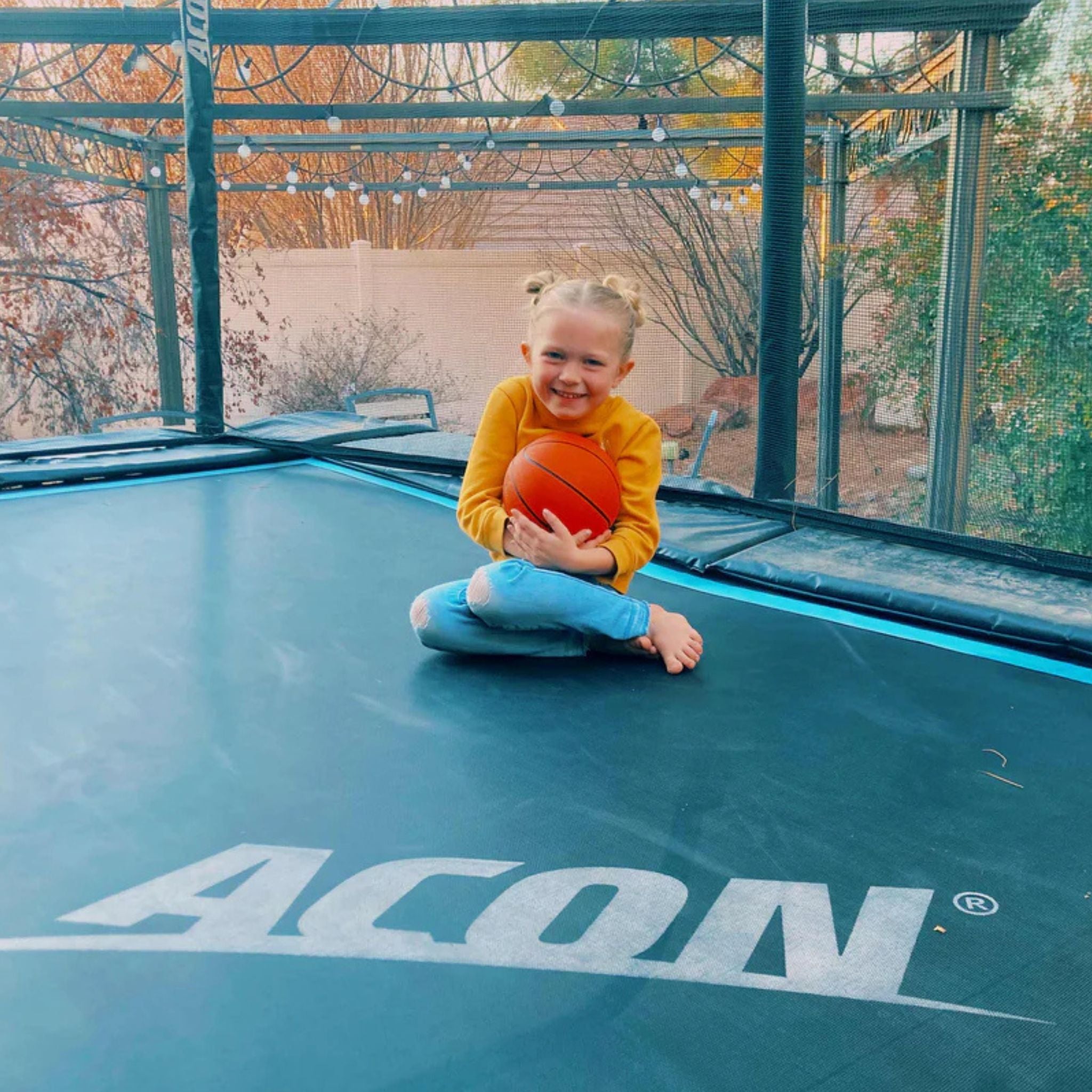 Kind sitzt mit Basketball einem Trampolin mit Lichtern