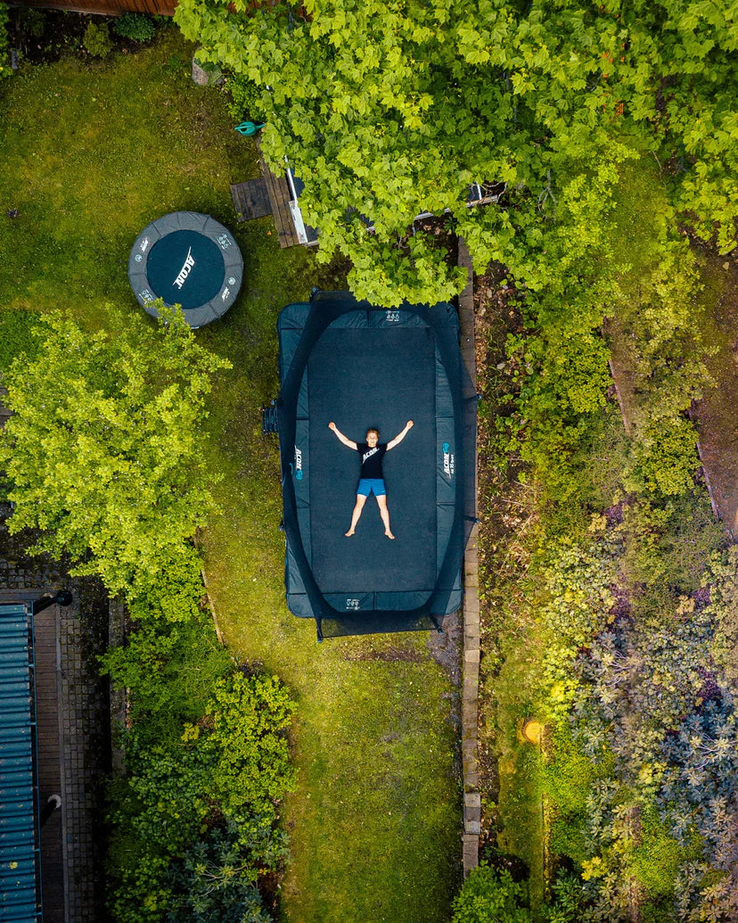 Kind liegt auf rechteckigem Trampolin im Garten
