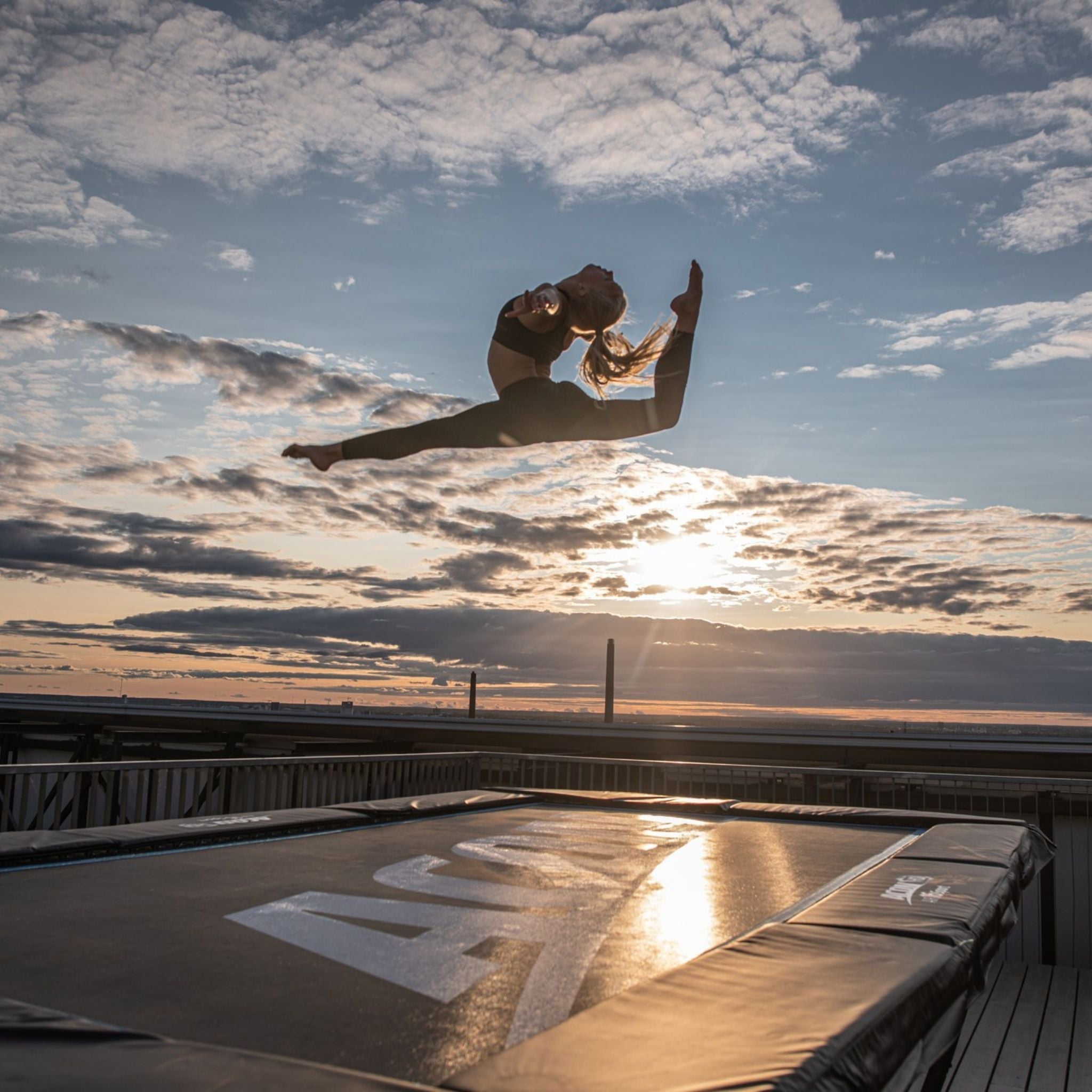 Frau springt auf dem Trampolin im Sonnenuntergang (auf dem Trampolin turnen)