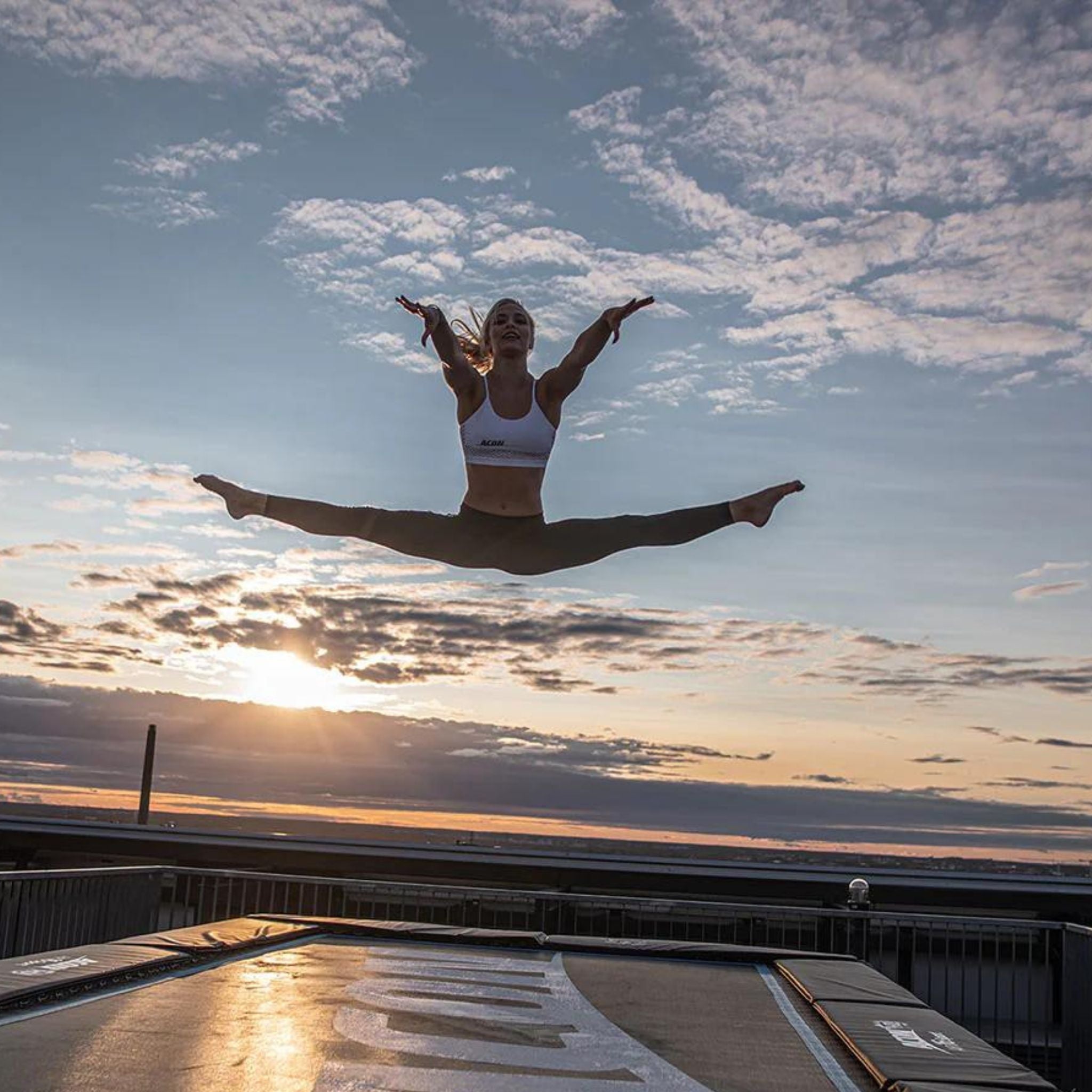 Schwangere Frau springt auf rechteckigem Trampolin im Sonnenuntergang. 