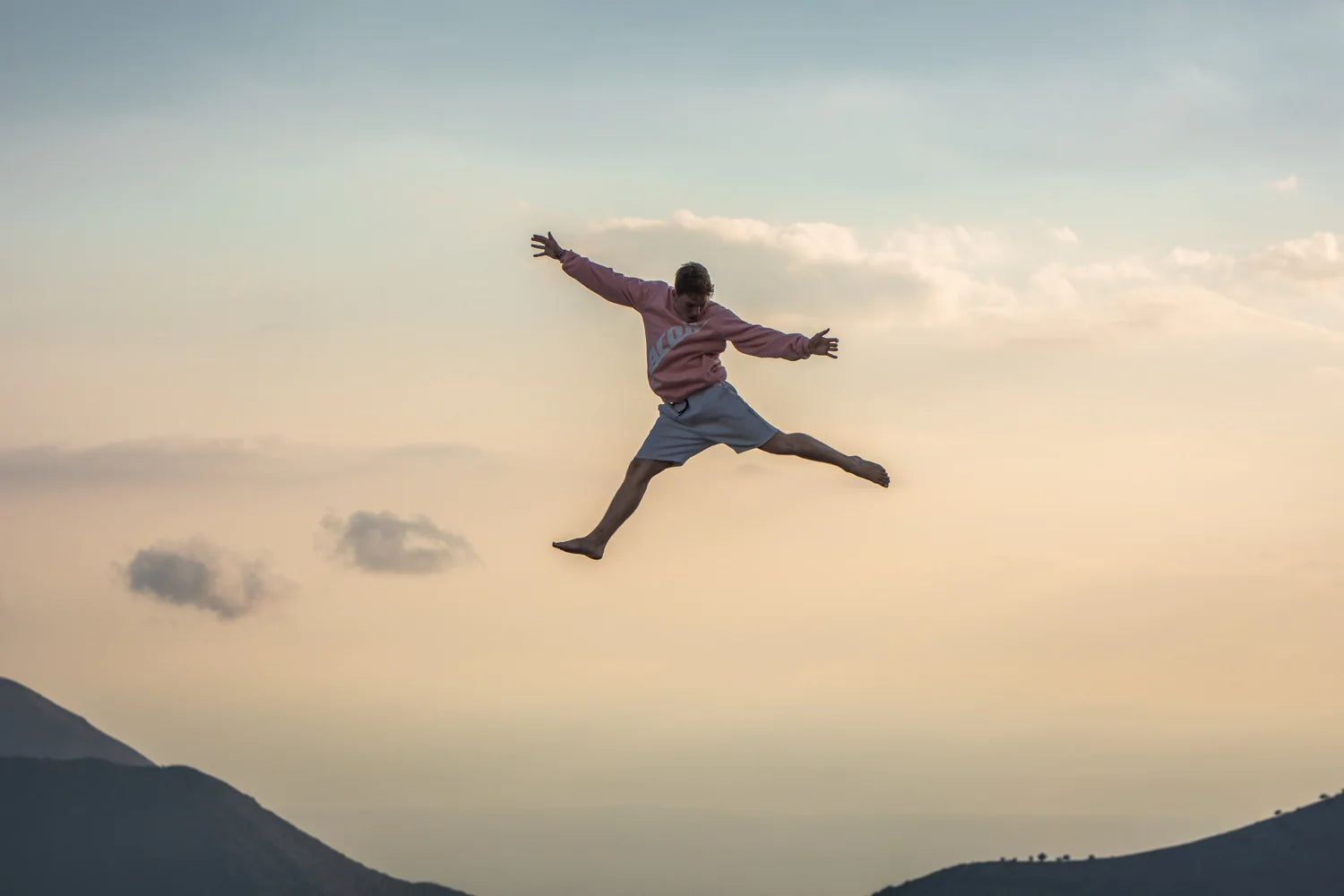 Eine Person, die in die Luft springt und ein rosafarbenes Acon-Sweatshirt in einer griechischen Landschaft trägt 