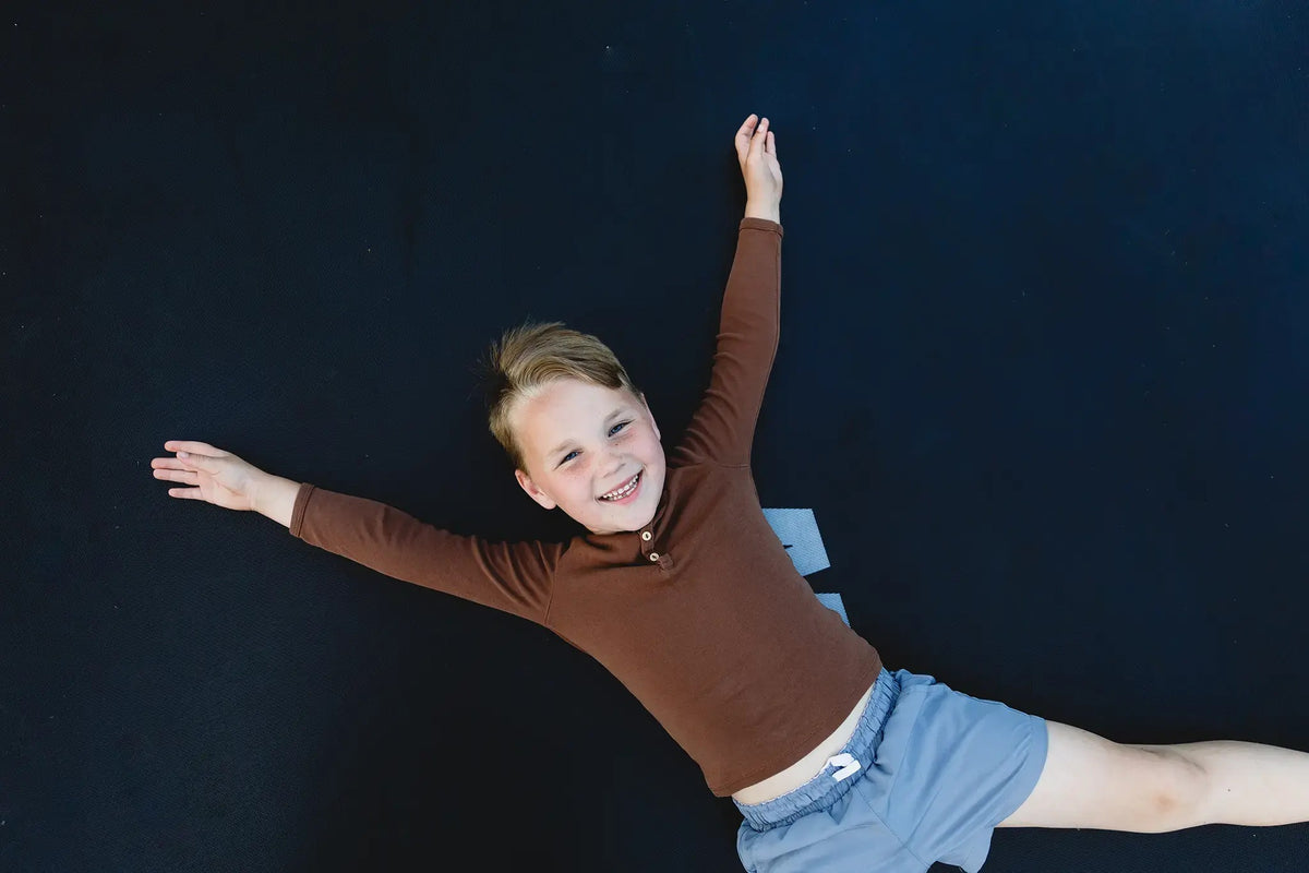 Ein fröhliches Kind liegt mit ausgebreiteten Armen auf einer schwarzen Acon-Trampolinmatte.