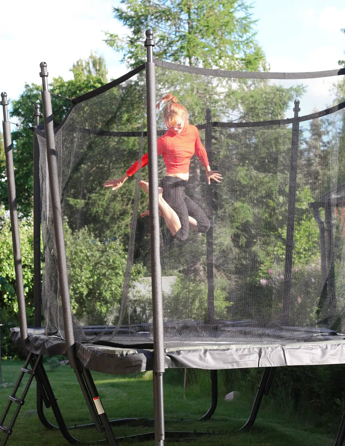Ein Teenager im roten Shirt in der Luft beim Springen auf einem Trampolin im grünen Garten.