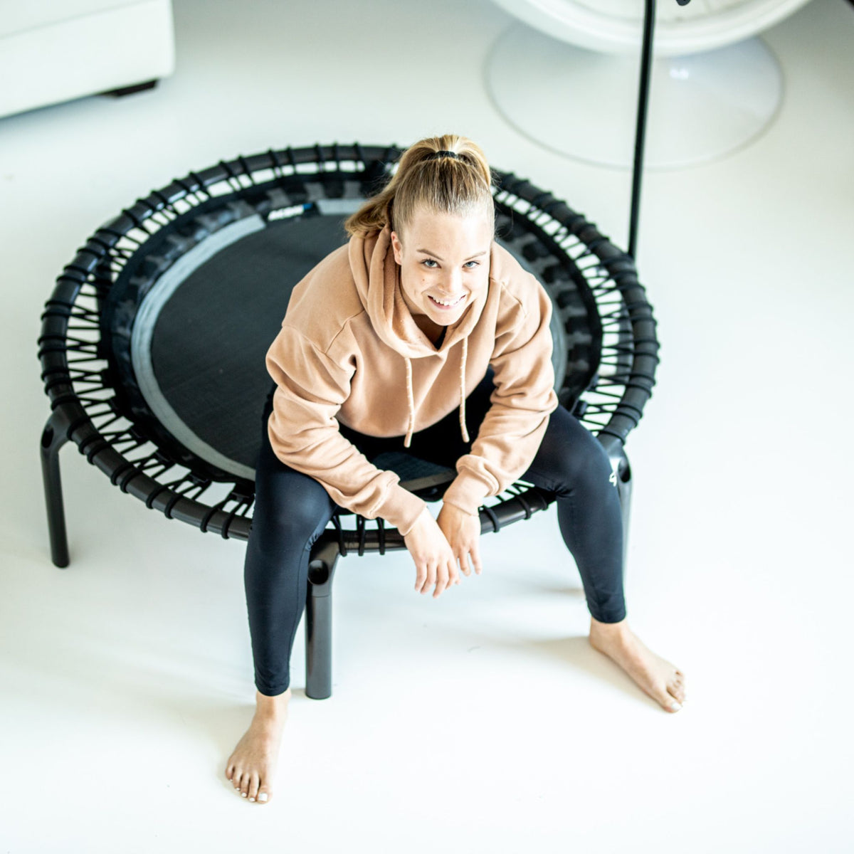 Eine Frau sitzt auf einem Trampolin in einem Raum, bereit für ihr Fitness-Training.
