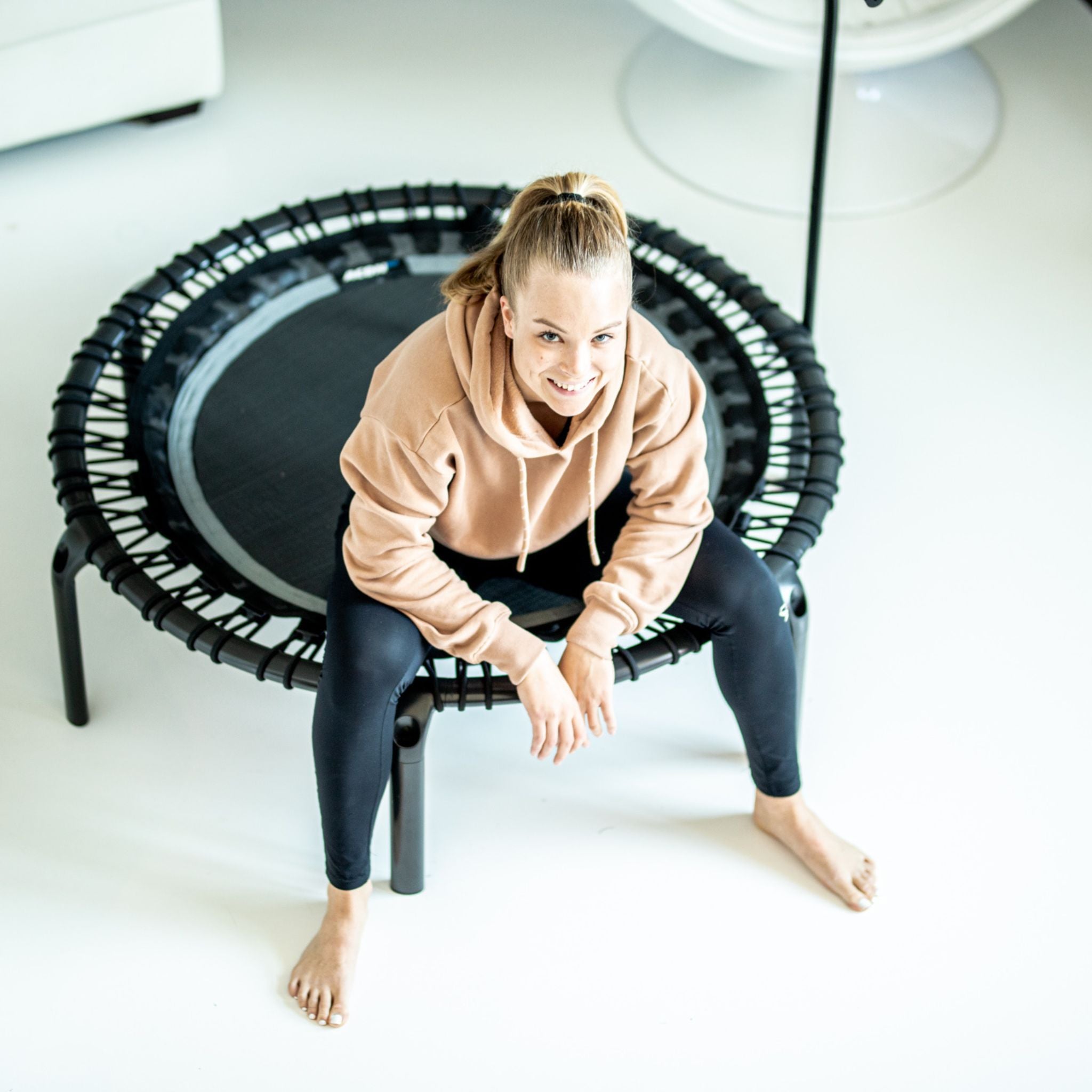 Eine Frau sitzt auf einem Trampolin in einem Raum, bereit für ihr Fitness-Training.