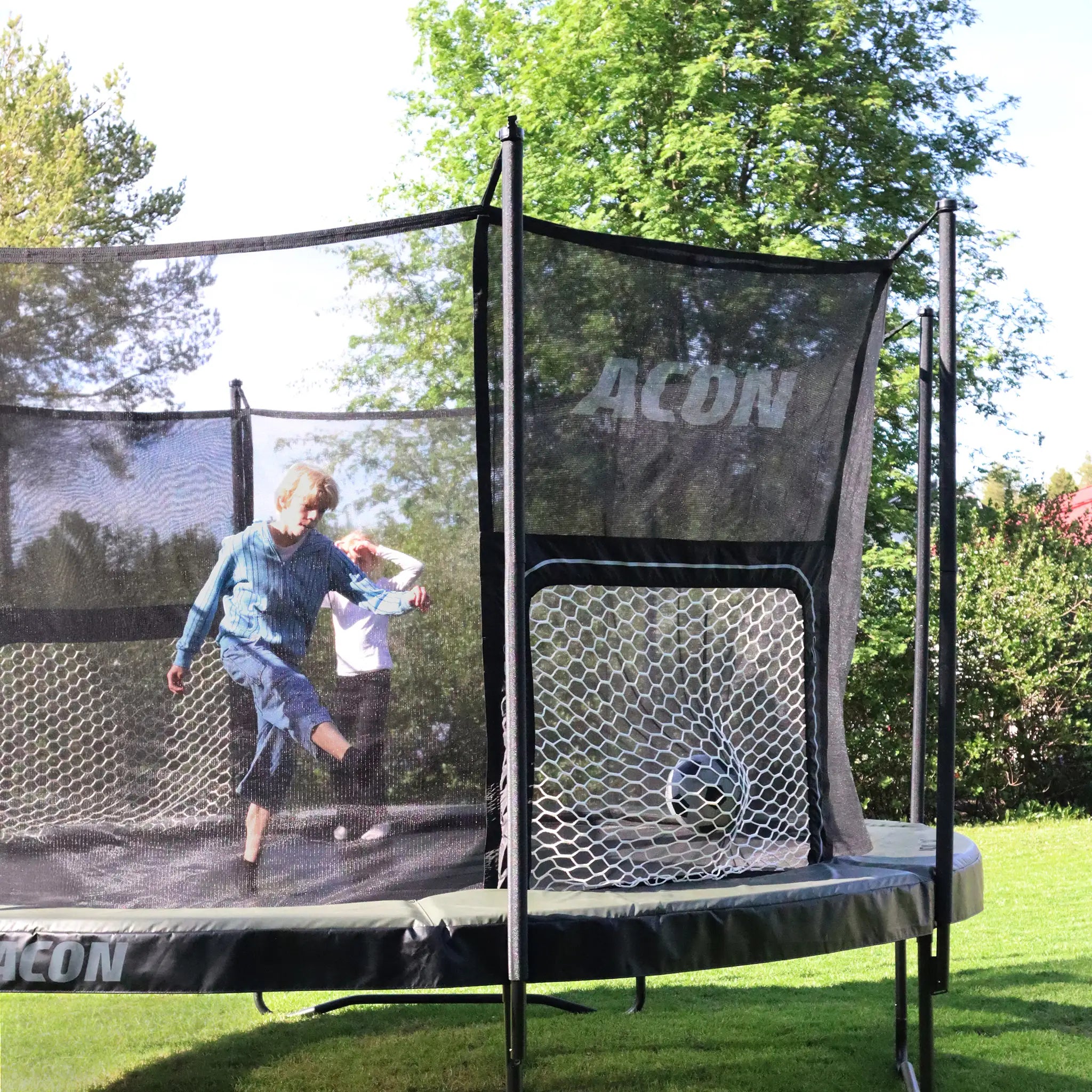 Kinder spielen Fußball auf einem ACON Air Rundtrampolin auf dem Rasen.