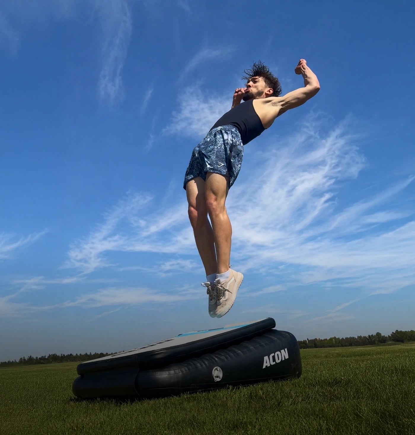 Ein Mann führt einen Backflip Launch auf einem Acon Airboard im Freien aus, das Airboard steht auf Gras.