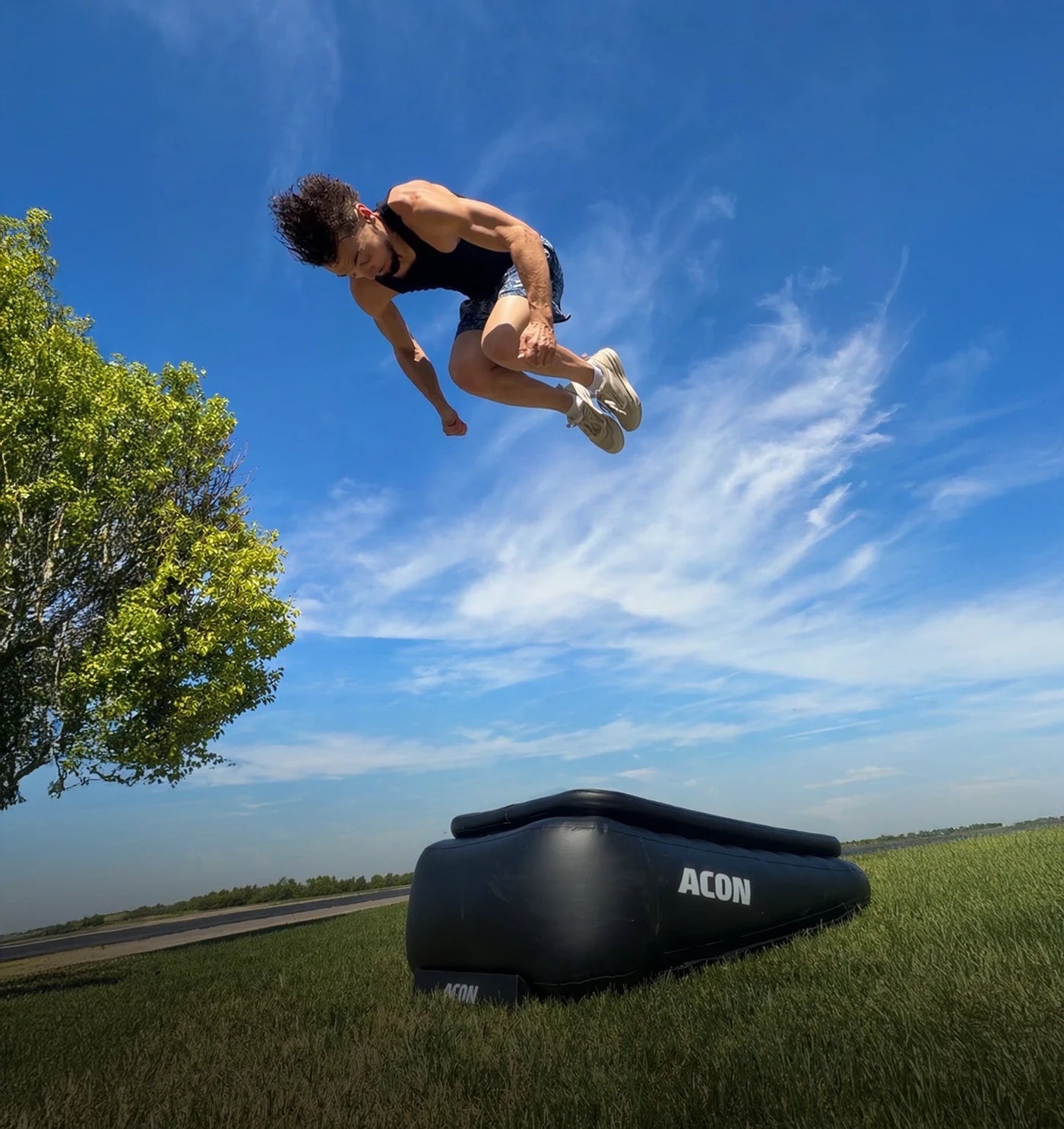 Ein Mann springt einen hohen Frontflip auf einem Acon Airboard im Freien, das Airboard steht auf Gras.