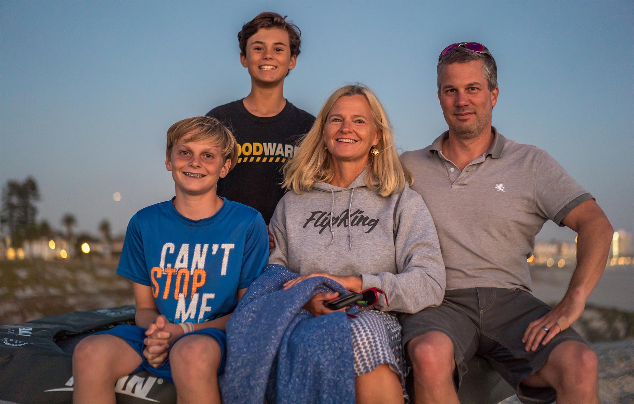 Acon-Kundenfamilie mit einer Mutter und drei Jungen, die am Strand sitzen