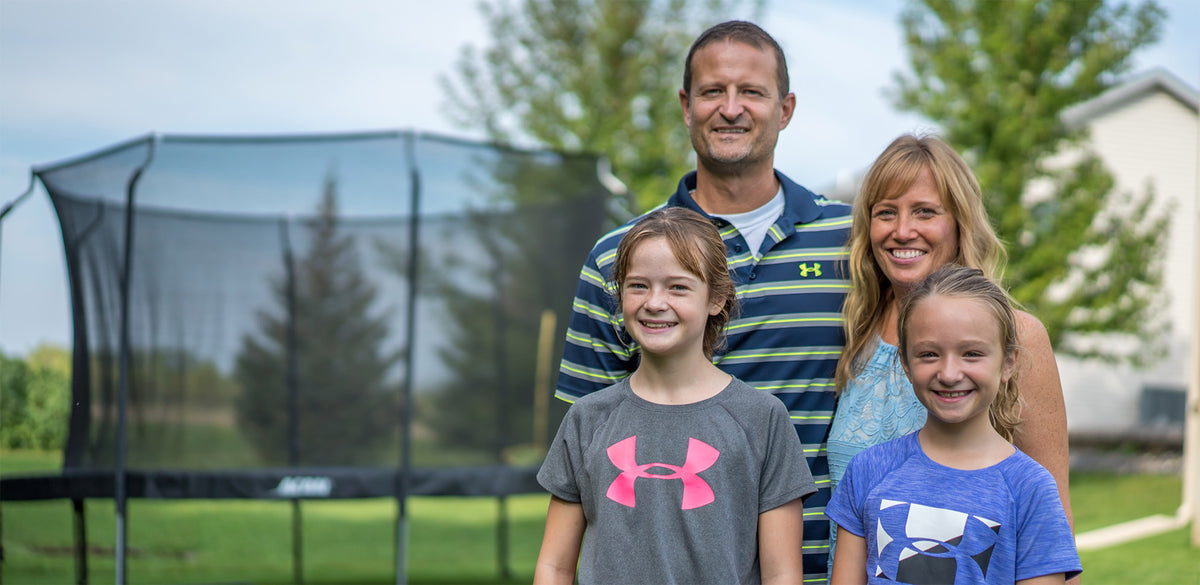 Acon-Kundenfamilie mit Vater und Mutter sowie zwei Mädchen. Im Hintergrund ist ein rundes ACON-Trampolin mit Netz