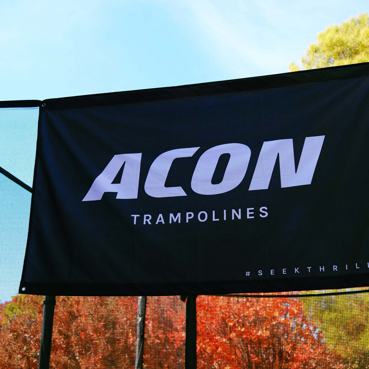 Nahaufnahme der schwarzen ACON-Flagge auf einem Trampolin vor dem Hintergrund bunter Blätter.