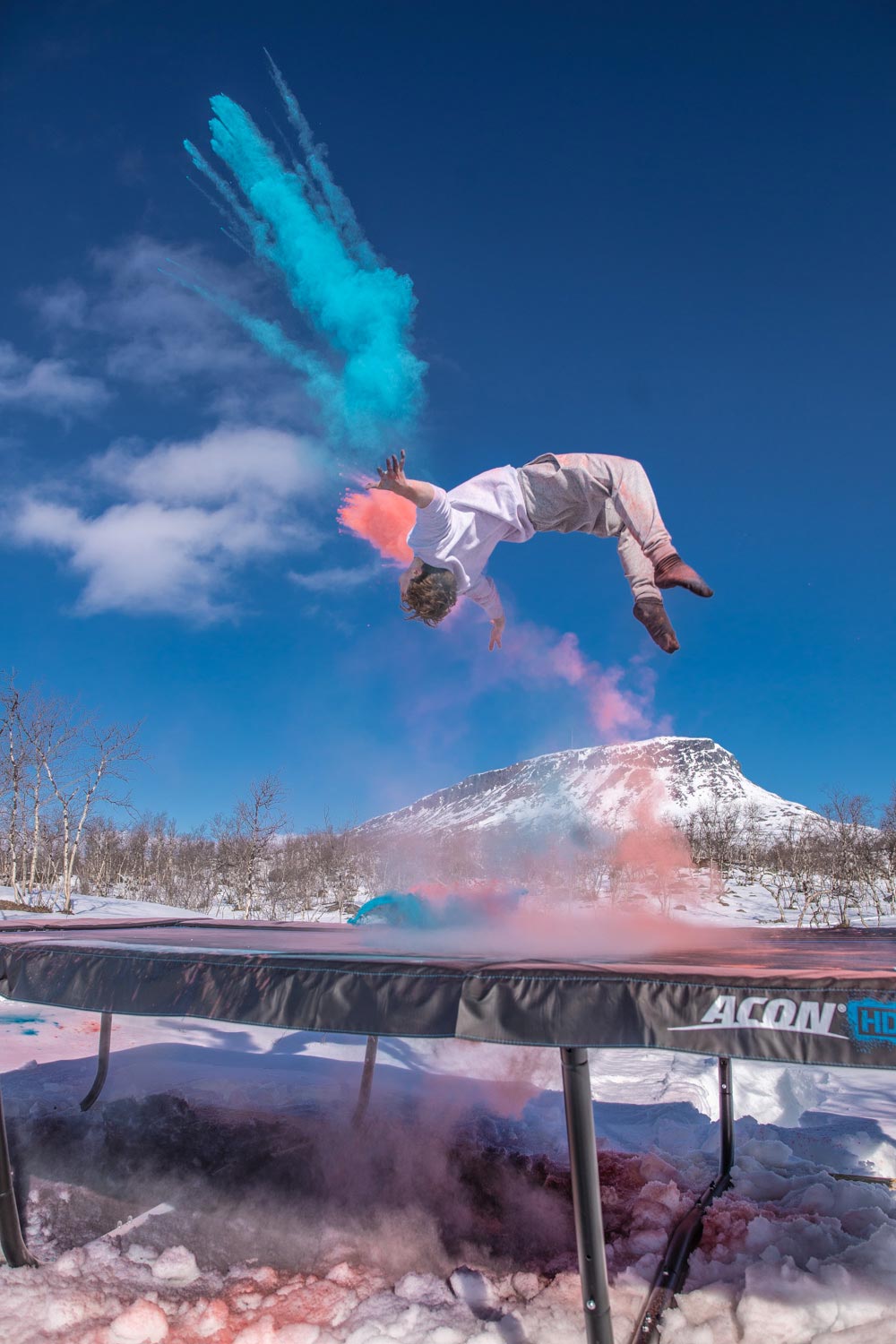 Eine Person springt auf einem ACON-Trampolin in Lappland, Finnland, während im Hintergrund rote und blaue Farben zu sehen sind 