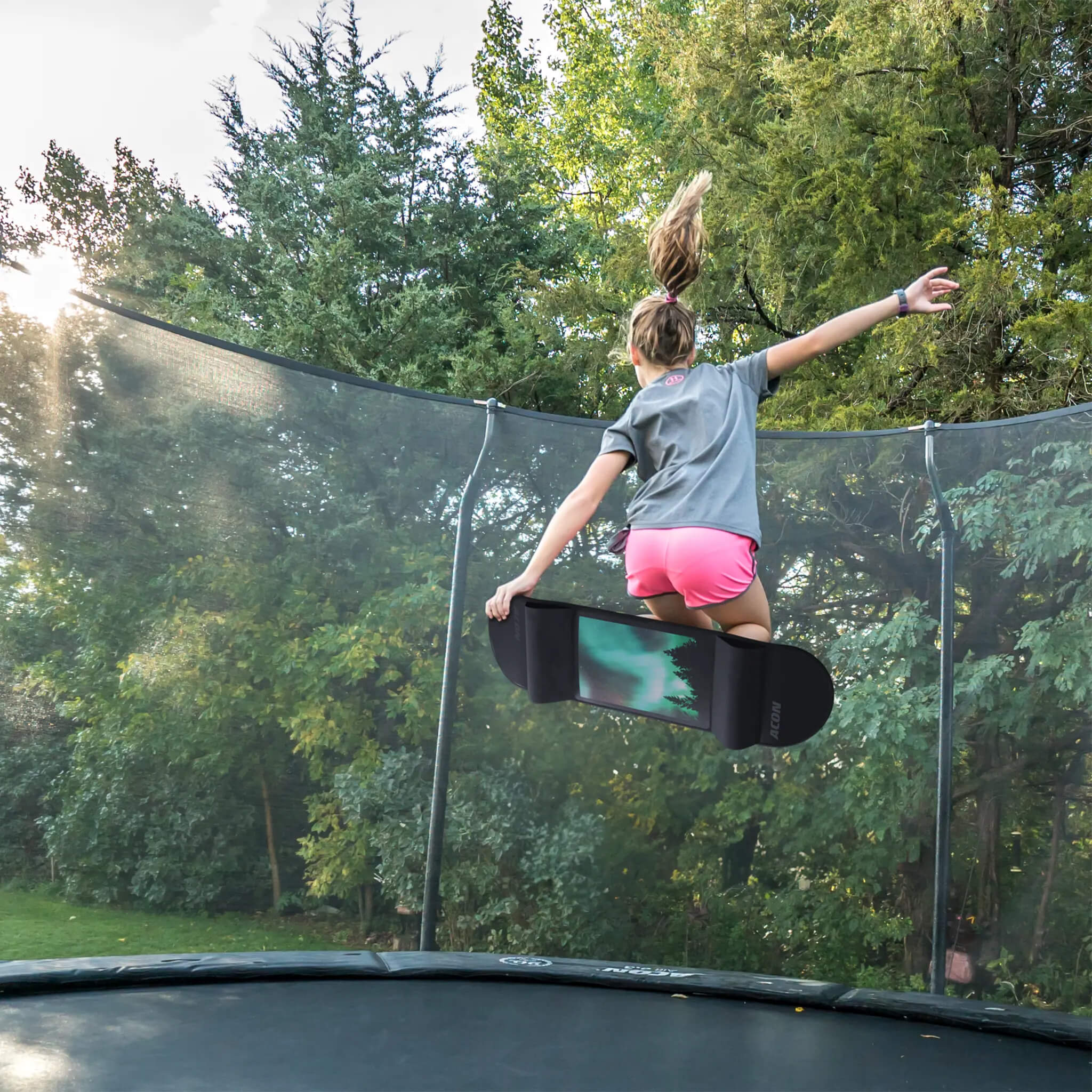Ein Mädchen springt auf einem Trampolin mit einem Acon Trampoline Skateboard.