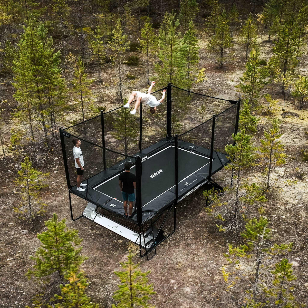 Drei Trampolintricker auf einem Acon X Trampolin in einem nordischen Kiefernwald.