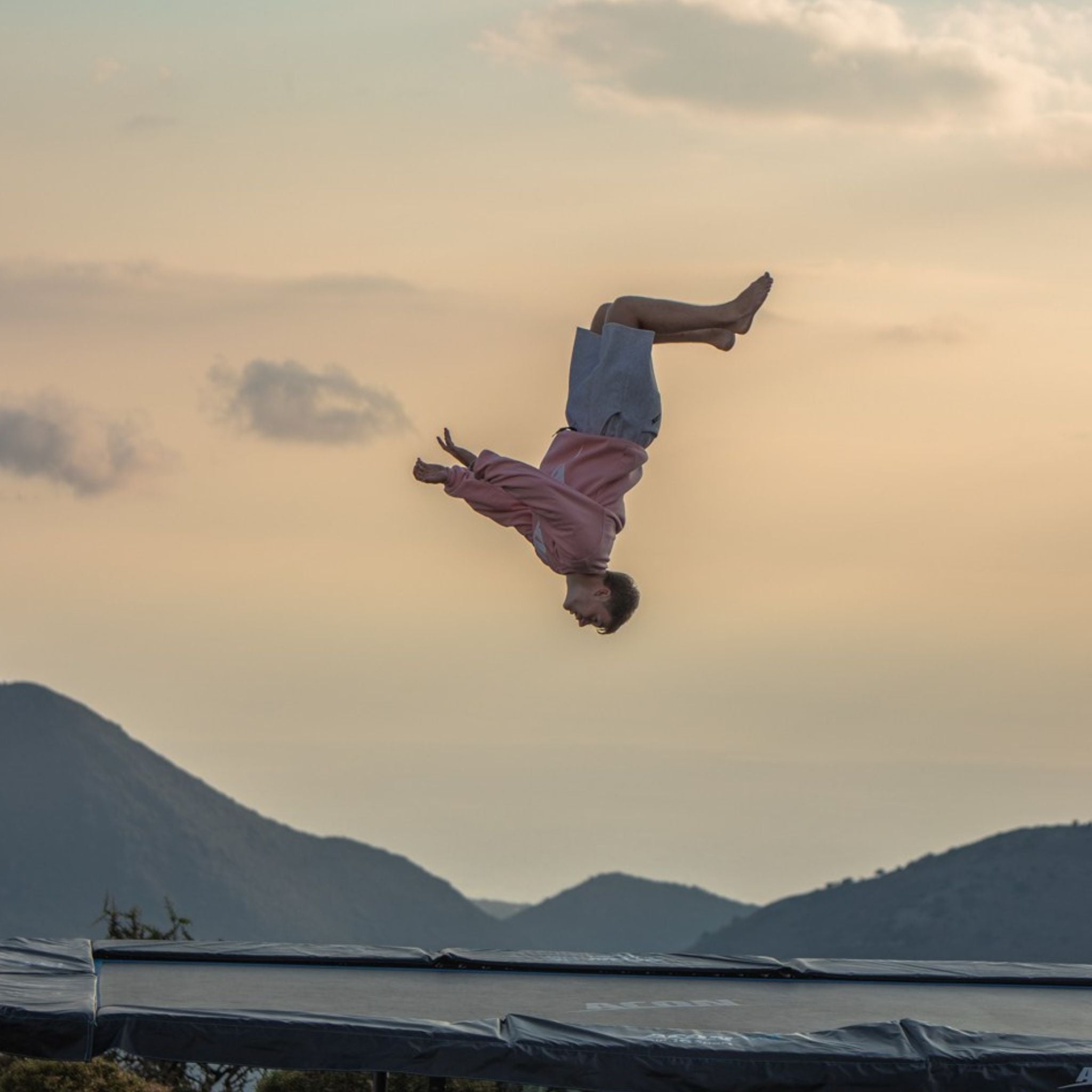 Mann macht Frontflip im Sonnenuntergang auf einem Trampolin