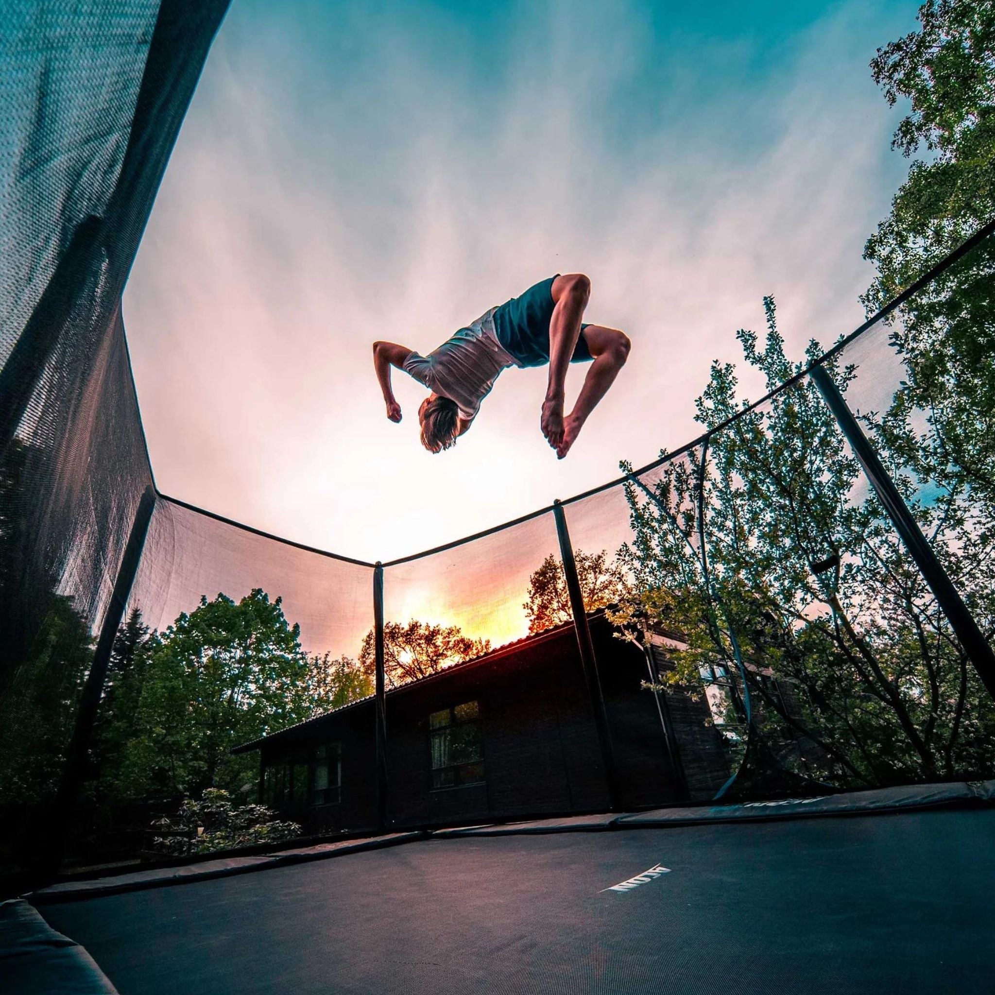 Mann macht Frontflip auf einem Trampolin im Sonnenuntergang