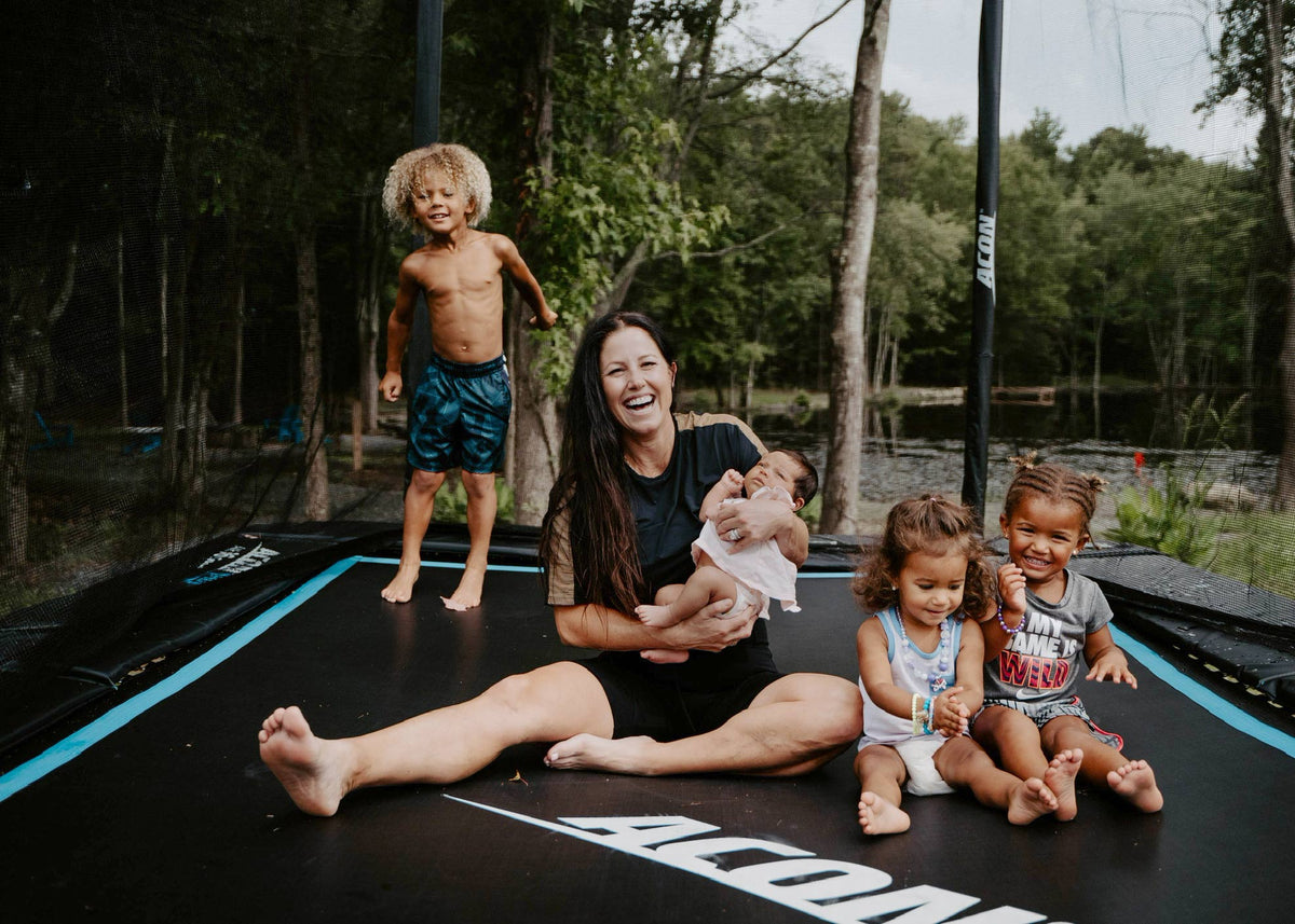 Mutter mit vier Kindern sitzt und lächelt auf dem Acon HD Trampolin 