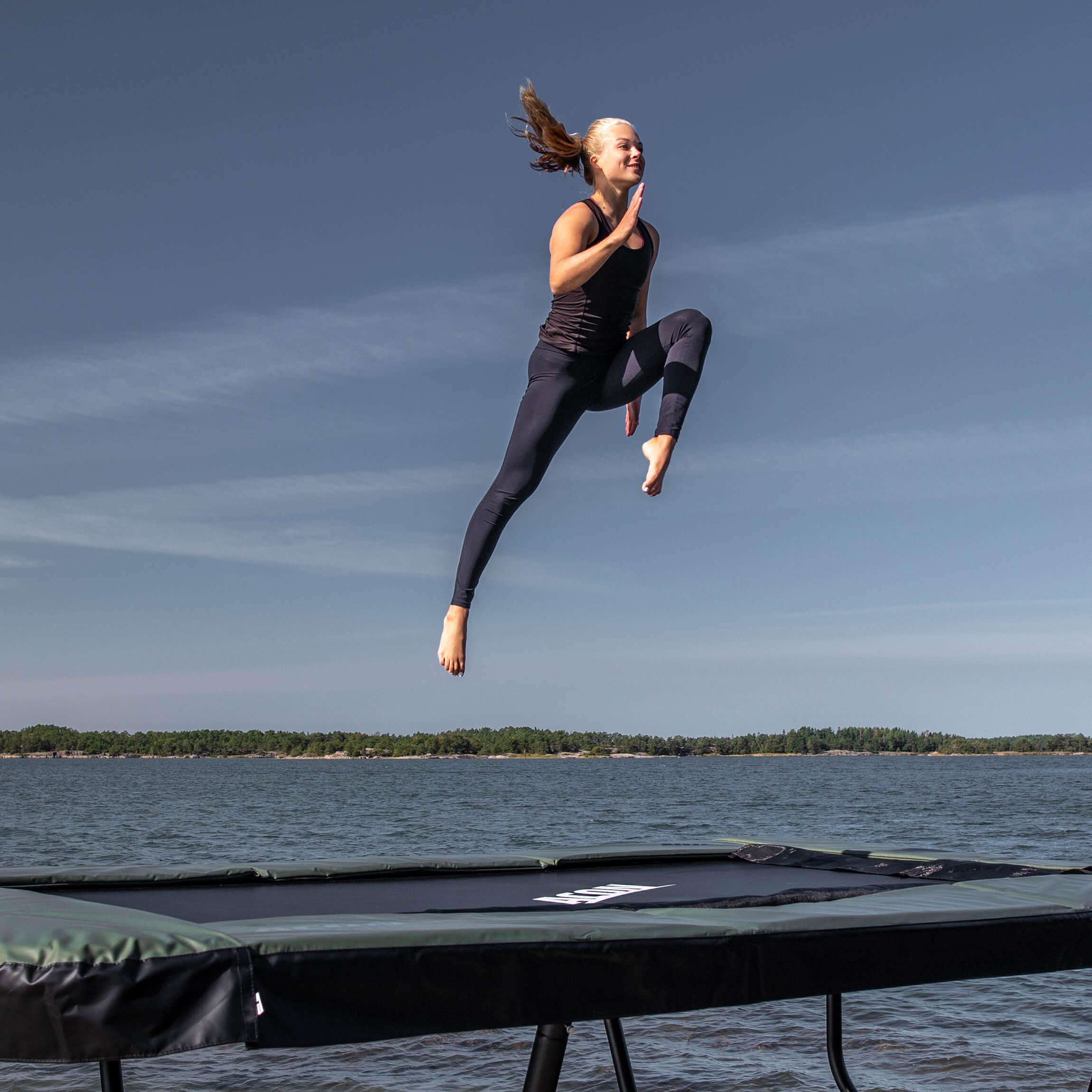 Ein Turner springt auf einem Acon 13 HD Trampolin in einer Schärenlandschaft.