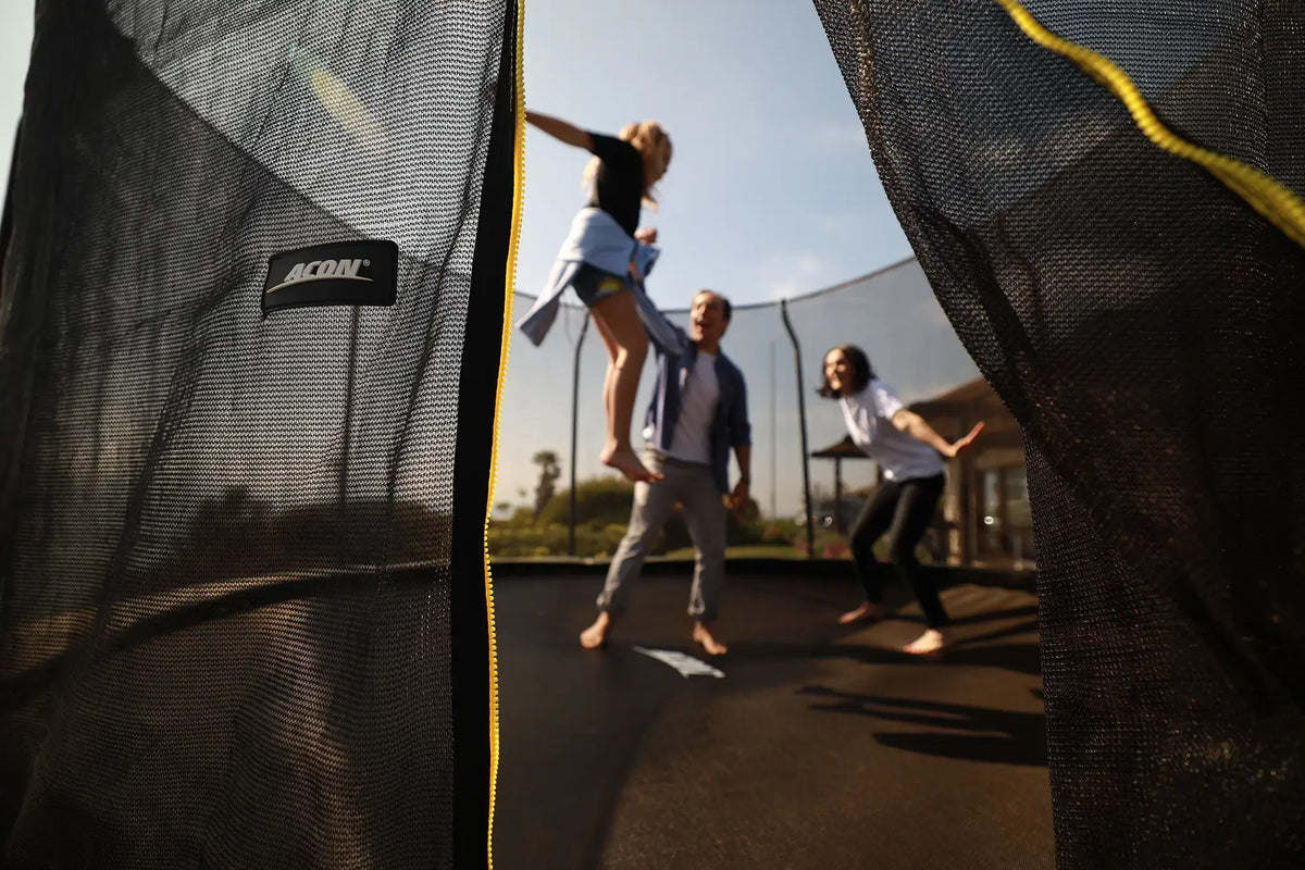 Familie spielt gemeinsam auf einem Acon-Trampolin, gesehen durch das Sicherheitsnetz.