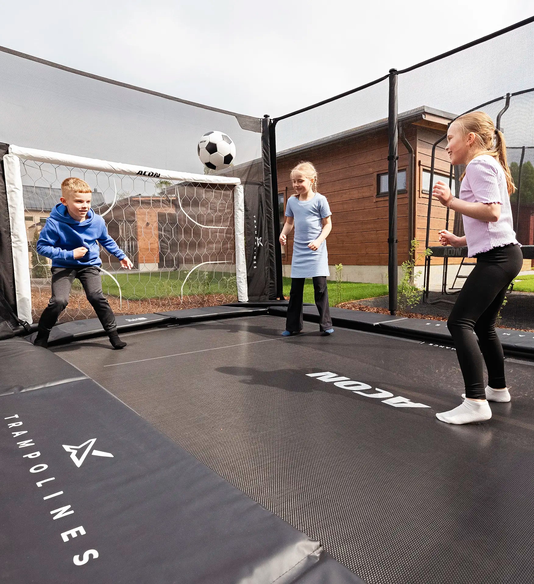 Kinder spielen mit einem Fußball auf einem Acon X 17ft Trampolin, im Hintergrund ein Fußballtor.