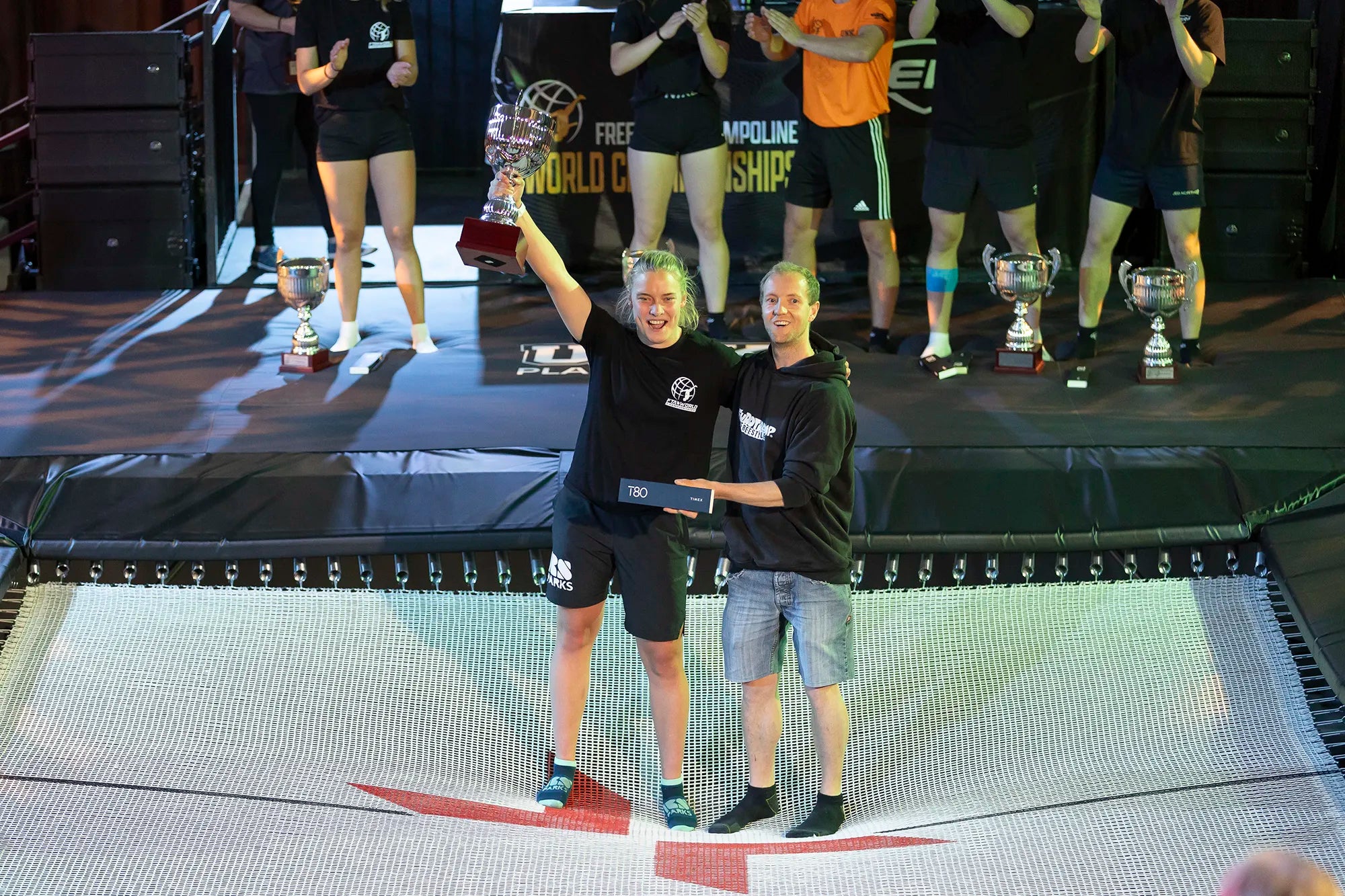 Der Sieger des Trampolinwettbewerbs hält einen Pokal auf dem Trampolin.