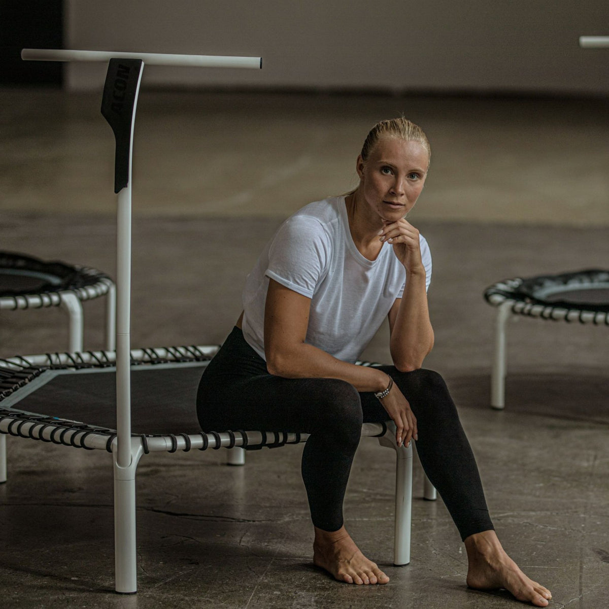 Frau in weißem T-Shirt sitzt auf Mini Trampolin