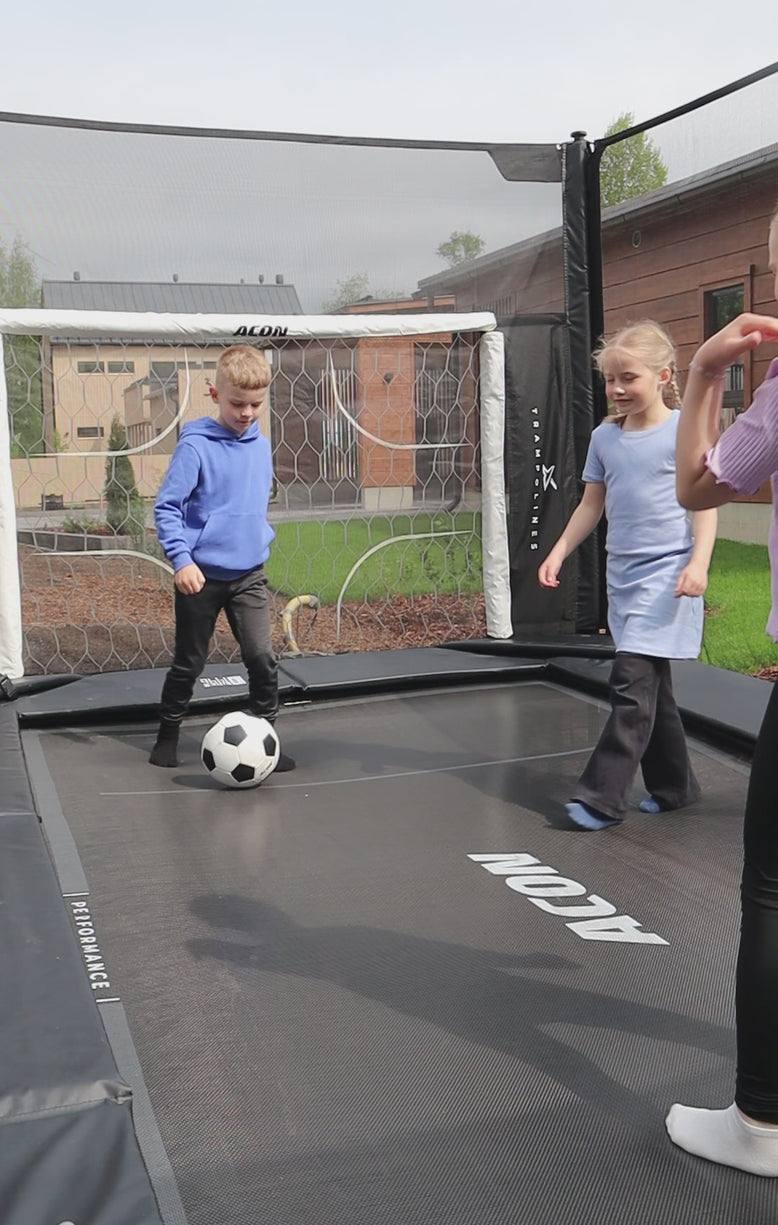 Drei Kinder spielen Fußball auf einem Acon X Trampolin. Hinter dem Torwart steht das Acon X Fußballtor.