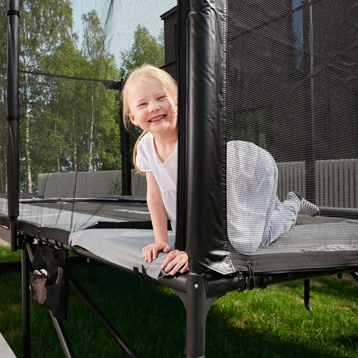 Ein junges Mädchen springt auf einem Trampolin im Garten, das sicher und stabil ist für unbeschwerten Spaß.