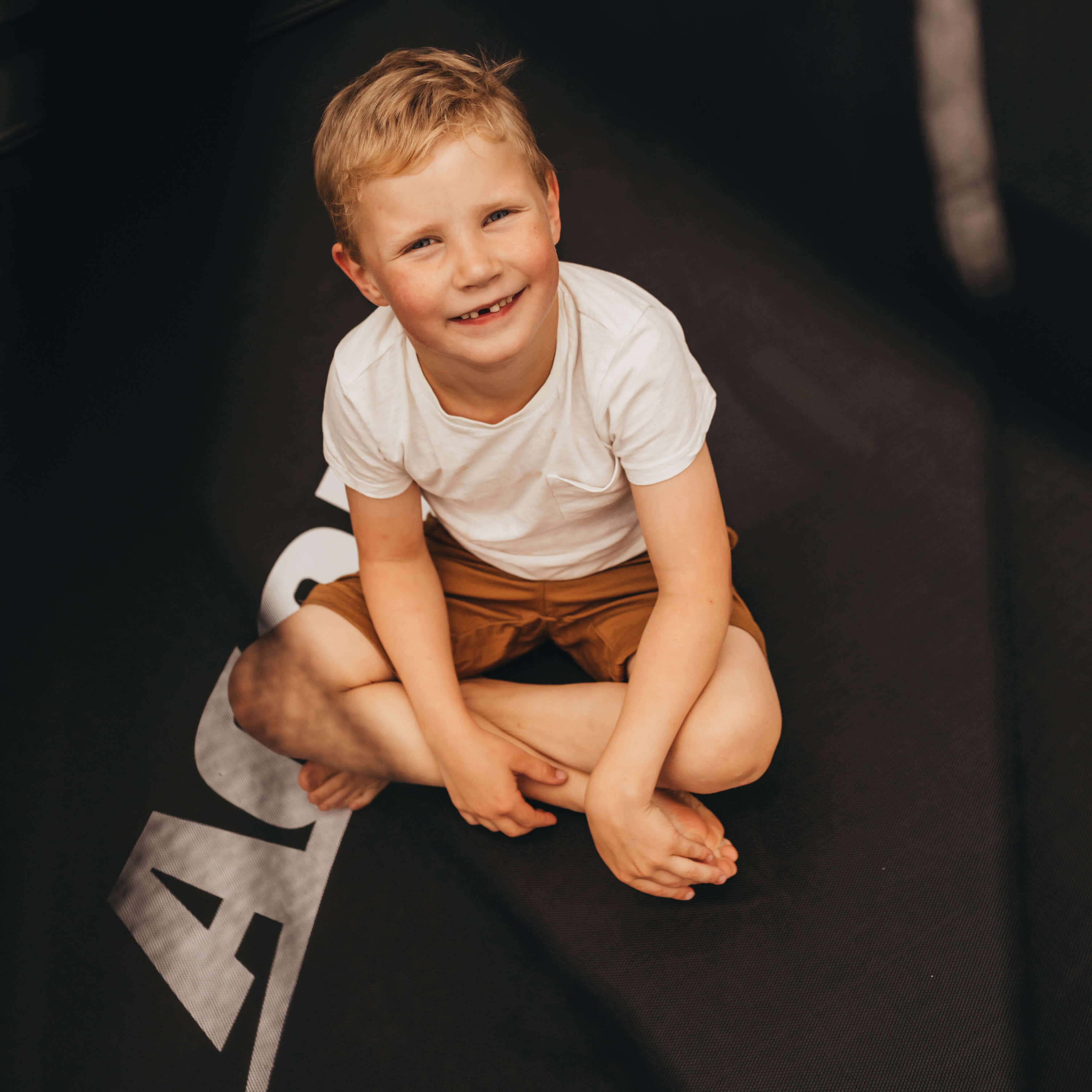 Ein lachender Junge sitzt auf einem Acon-Trampolin.