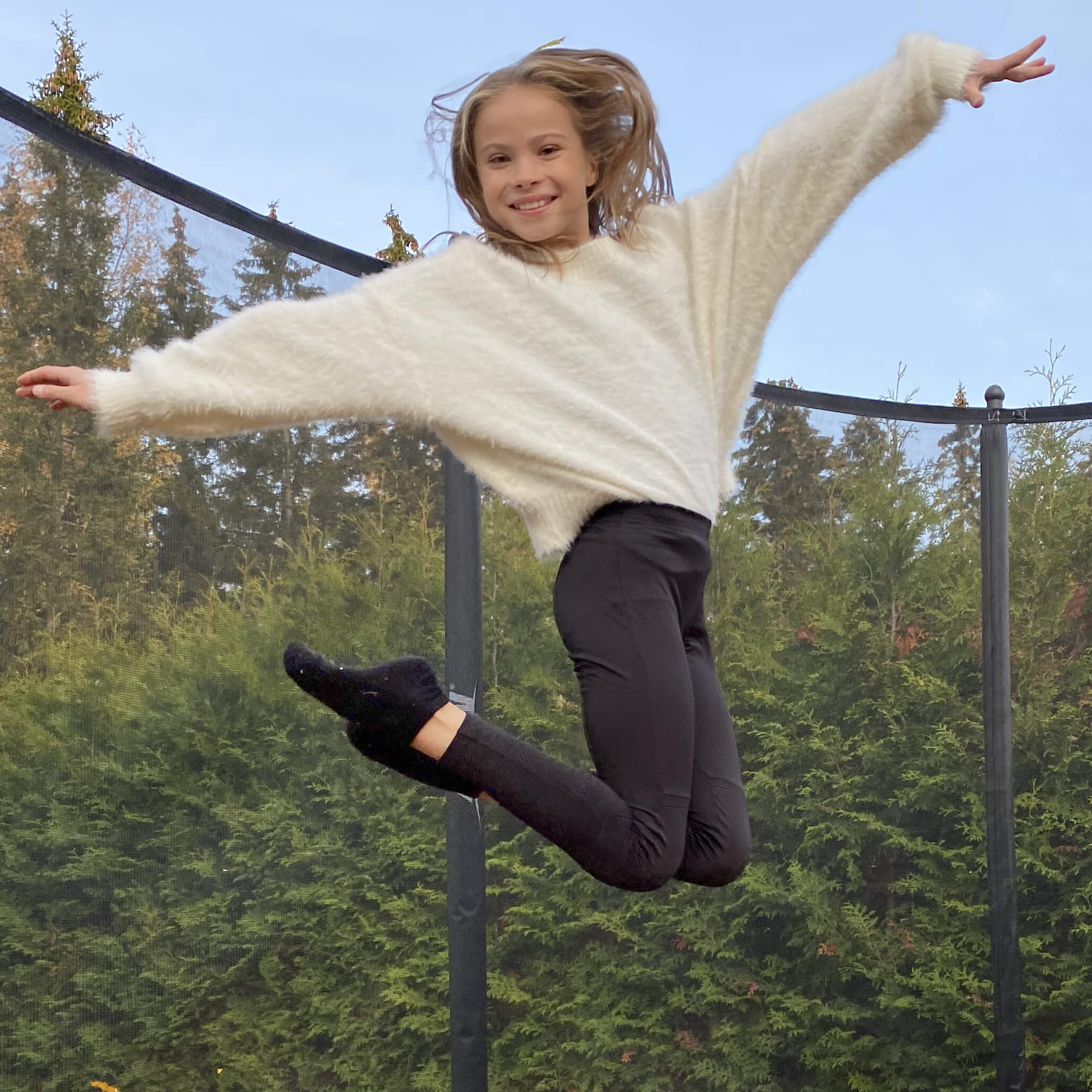 Ein lächelndes Mädchen springt auf einem Acon-Trampolin mit Sicherheitsnetz