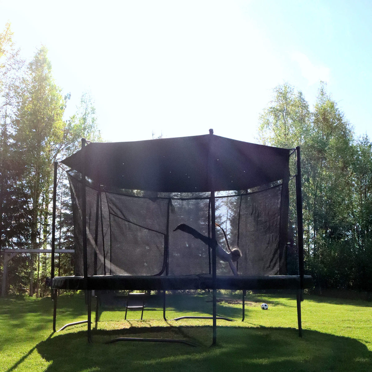 Acon Air Rundtrampolin mit Sonnenschutz in einer sonnigen Outdoor-Umgebung, ein Kind springt.